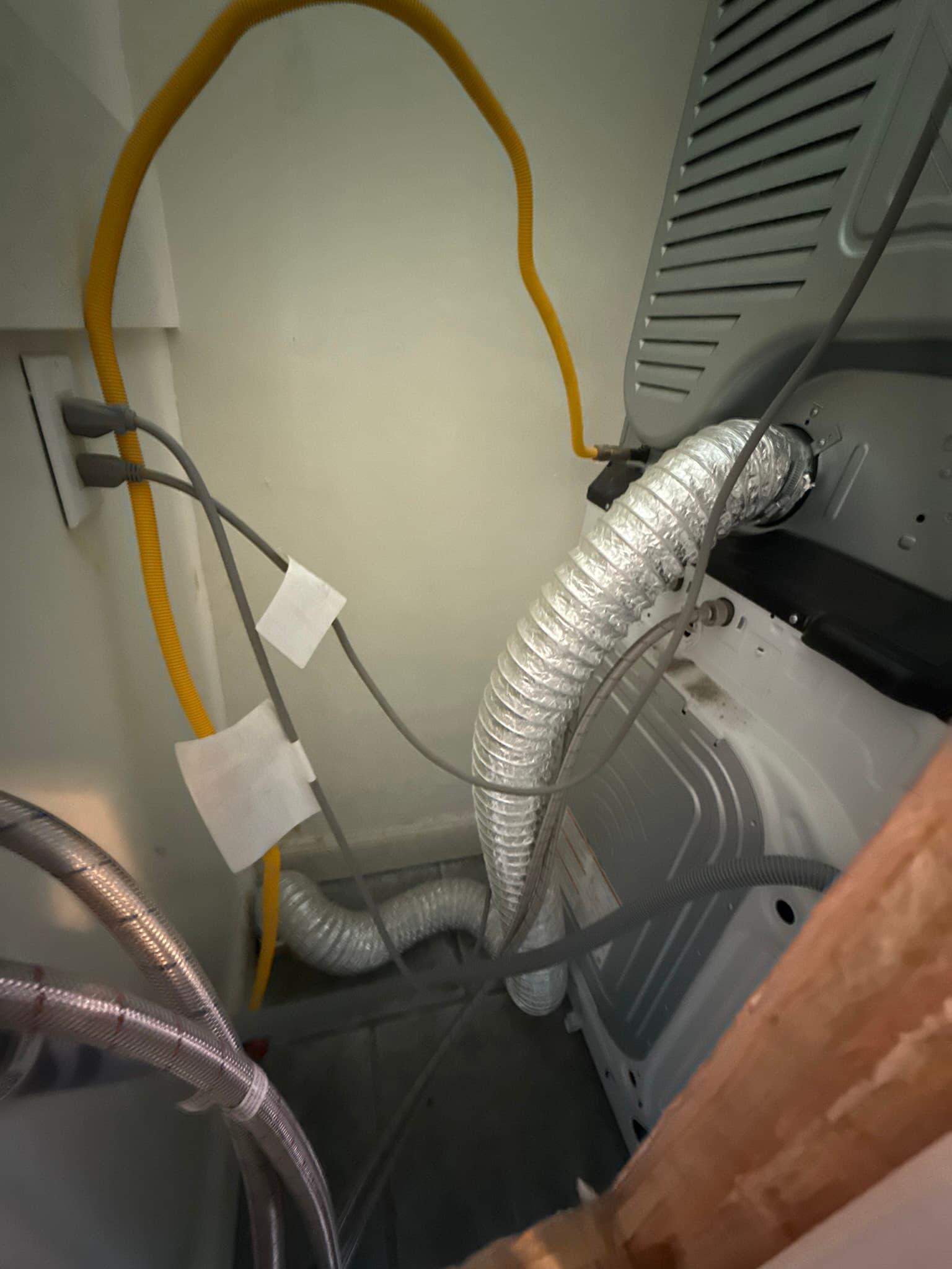 Close-up view of a dryer exhaust duct connection showing the duct condition and connection hardware at the back of the appliance