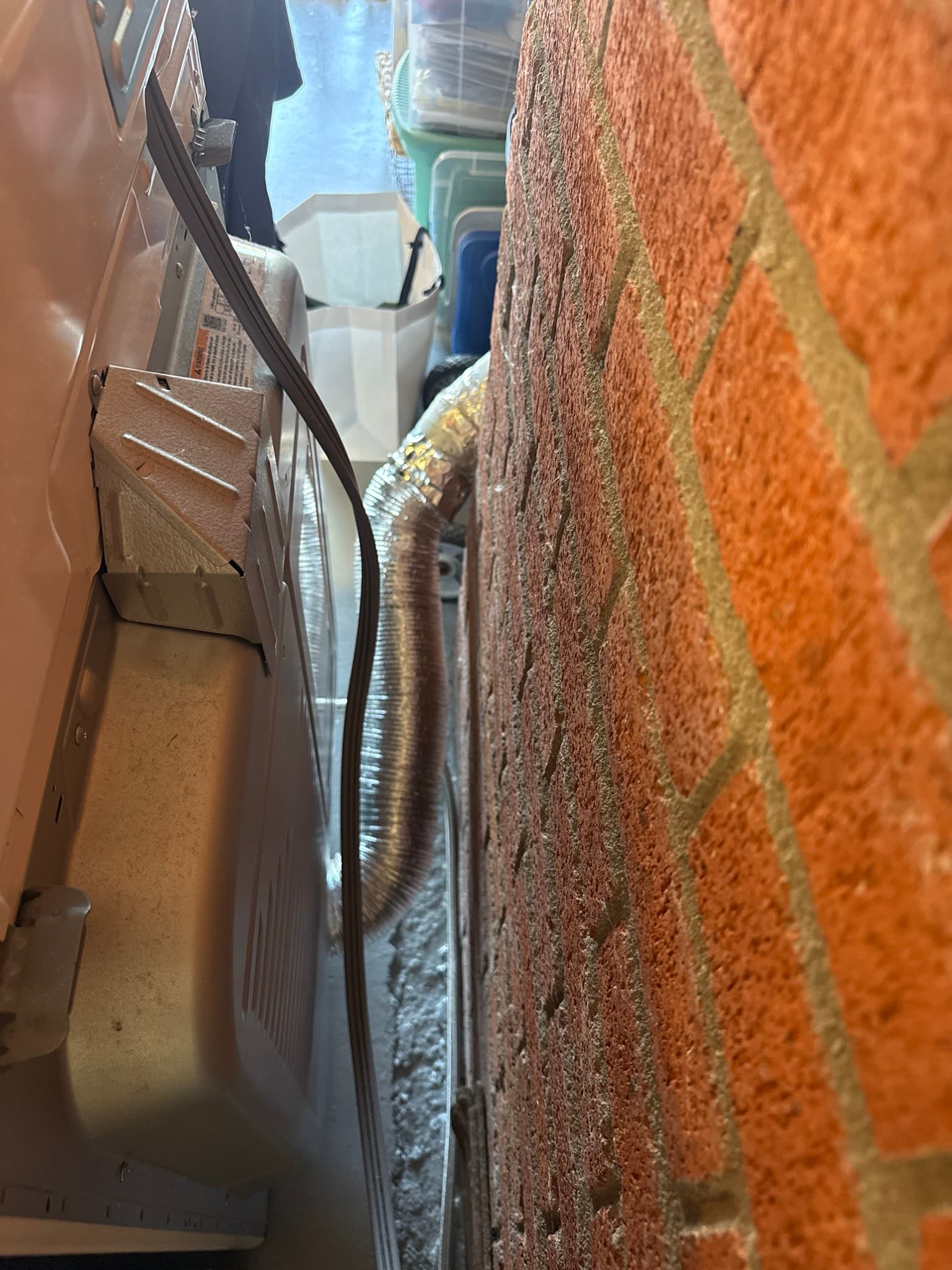 Exterior dryer vent duct running horizontally along a red brick wall with visible lint accumulation along its length and moisture or condensation on the duct surface near an algae-stained vent cap area