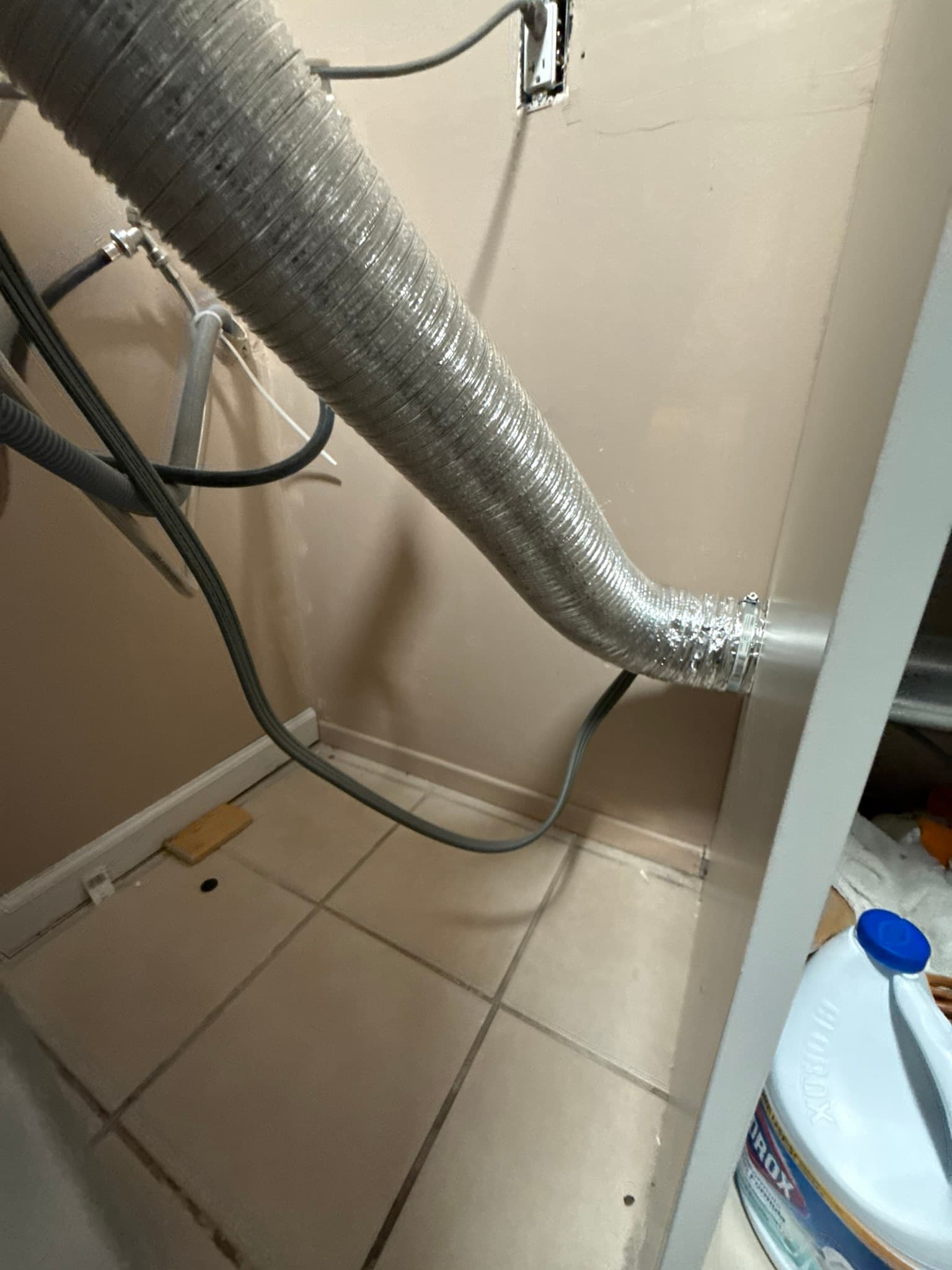A DryerFlex UL 2158A-listed semi-rigid aluminum transition duct installed behind a dryer, running from the dryer exhaust outlet upward toward the wall connection.