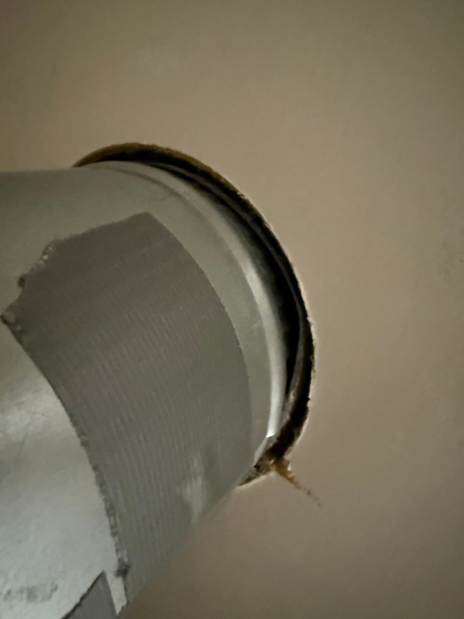 A flexible dryer vent duct with visible dark lint accumulation along the outer surface and at the clamp area, with gaps visible at the duct connection indicating poor sealing.
