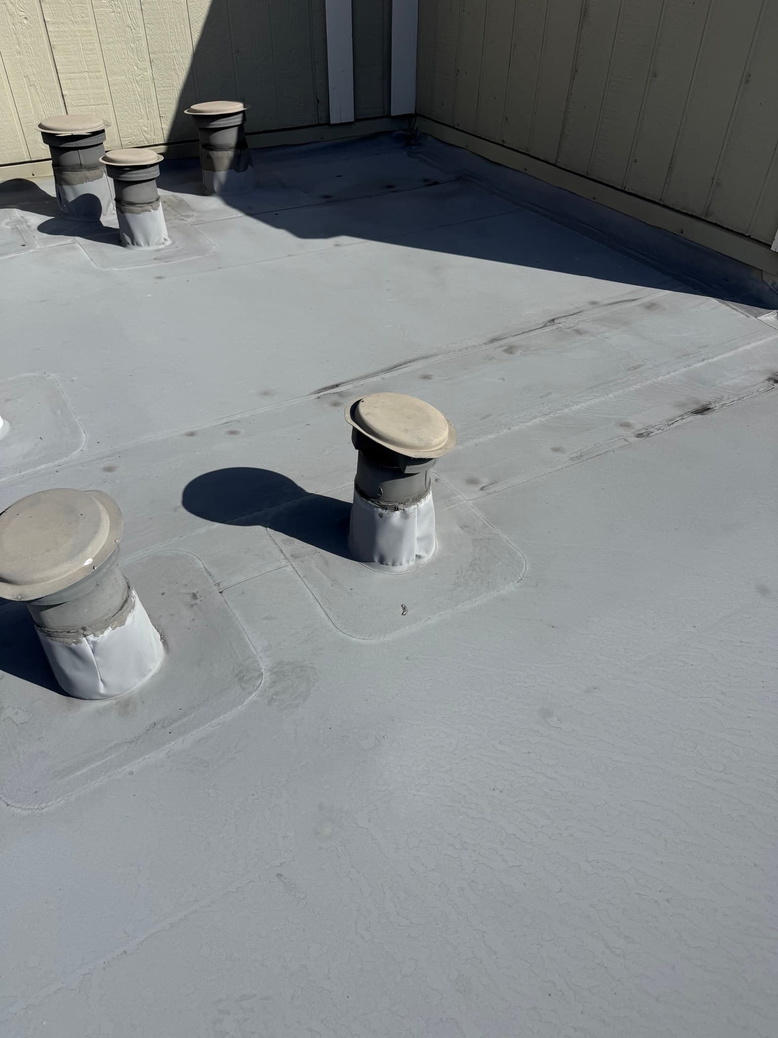 Multiple cylindrical vent caps with dome-style tops installed through a flat white roof membrane, with rectangular base boots sealed to the roof surface and minor soiling visible around some penetration bases.