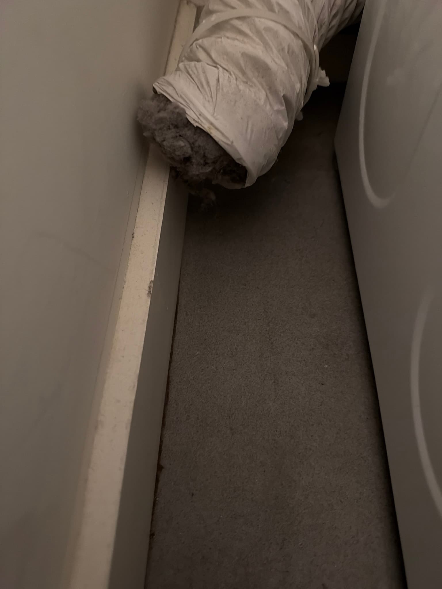 White plastic accordion-style flexible transition duct behind a dryer with heavy lint clogging its open end
