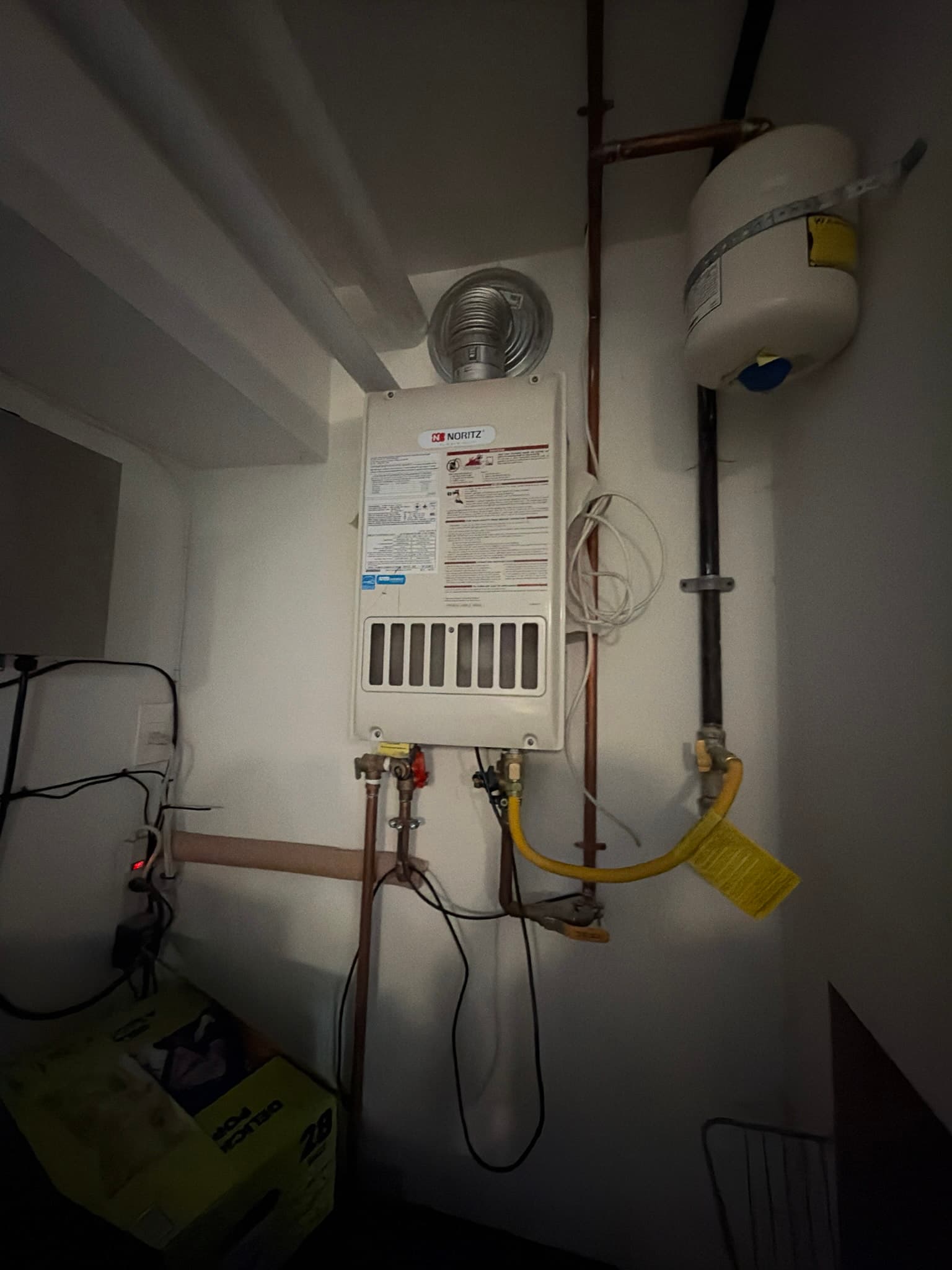Wall-mounted tankless water heater with intake and exhaust vent cap, copper and gas line connections, isolation valves, and an expansion tank on the supply line