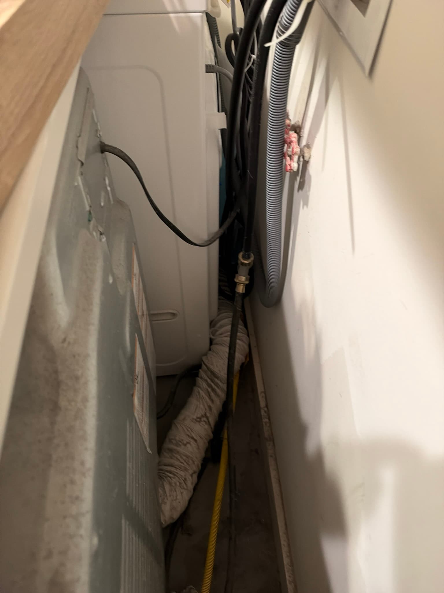 Dryer positioned tight against a wall with a heavily soiled flexible transition duct running through a cramped gap alongside gas, electrical, and water supply lines