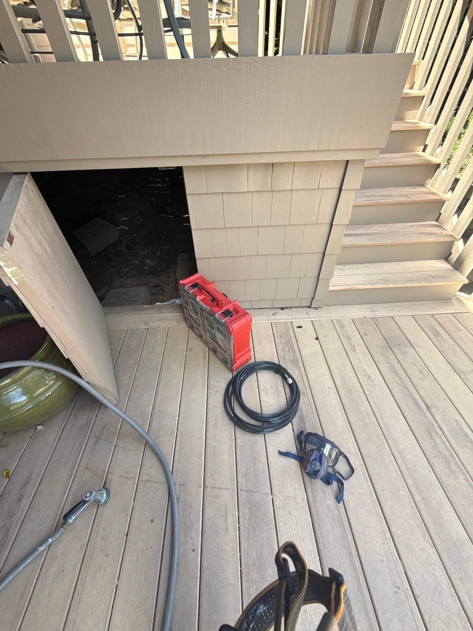 Exterior dryer vent opening on a residential deck in Menlo Park showing a dark interior cavity and no visible backdraft damper, with a red motorized brush unit and coiled black cleaning cable staged on the deck in front of the vent in preparation for service