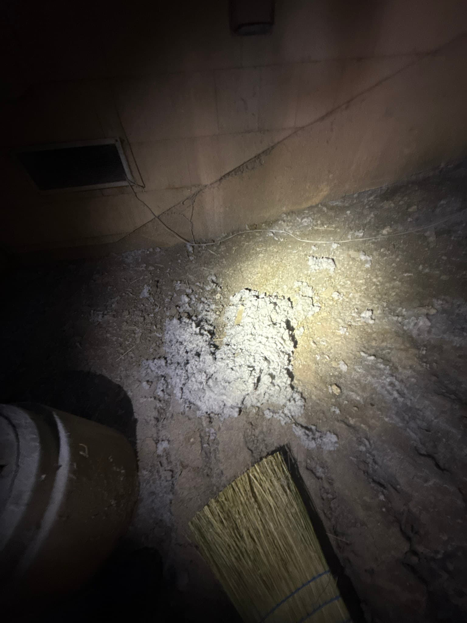 Interior of a dryer exhaust duct showing thick white and gray compacted lint coating the duct walls and floor, with a cleaning brush tool visible at the lower right and a flexible duct section at the upper left, captured during the cleaning process