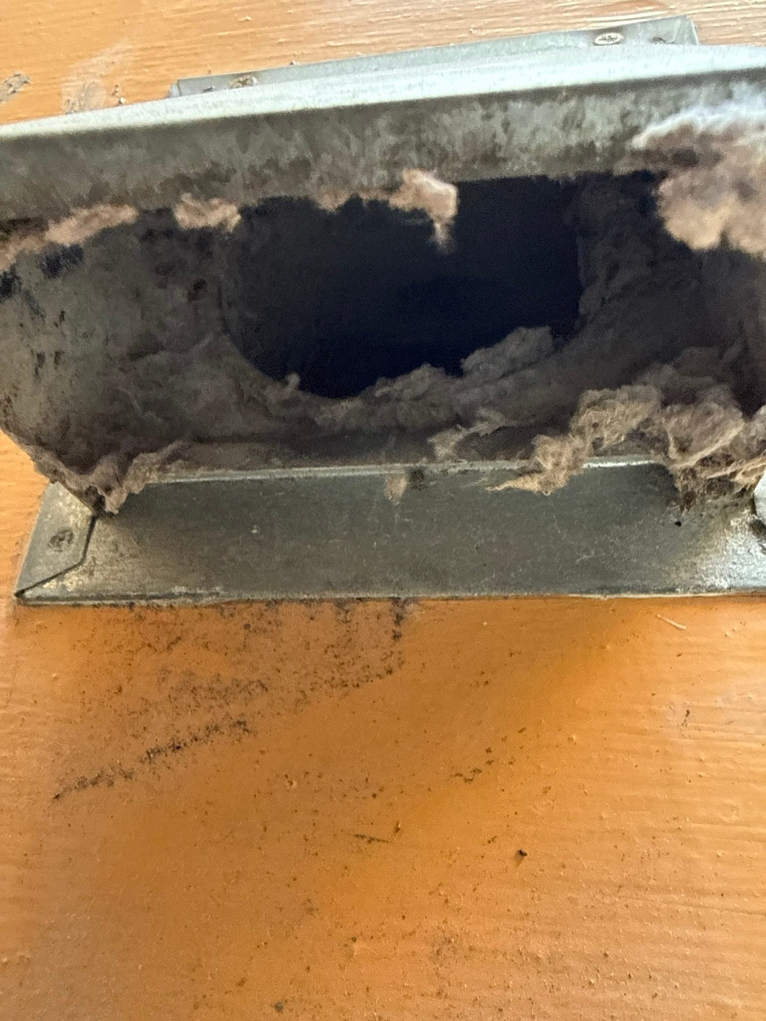 Dryer lint trap chamber with severely compressed lint buildup completely blocking the interior opening and coating the metal housing walls and bottom panel.
