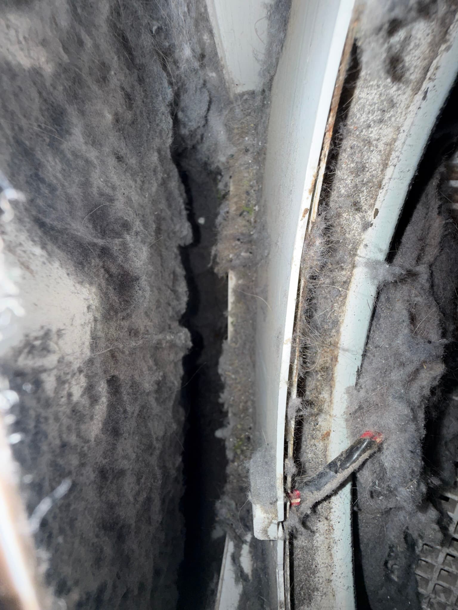 Interior view of a metal dryer exhaust duct showing densely packed lint matting along both side walls, with only a narrow central airflow channel remaining