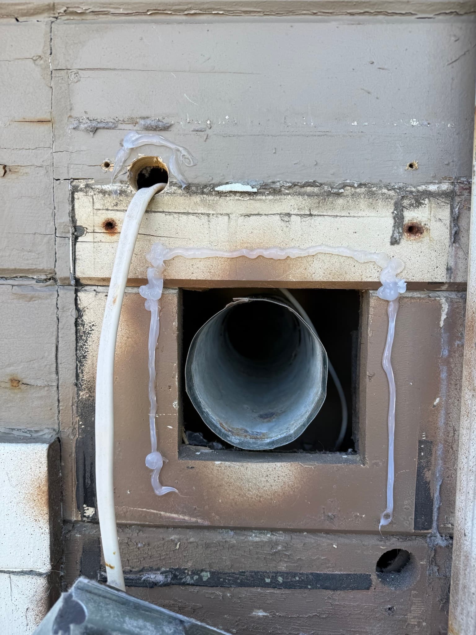 View along an exposed rigid dryer exhaust duct in a residential garage showing duct supports and joint connections