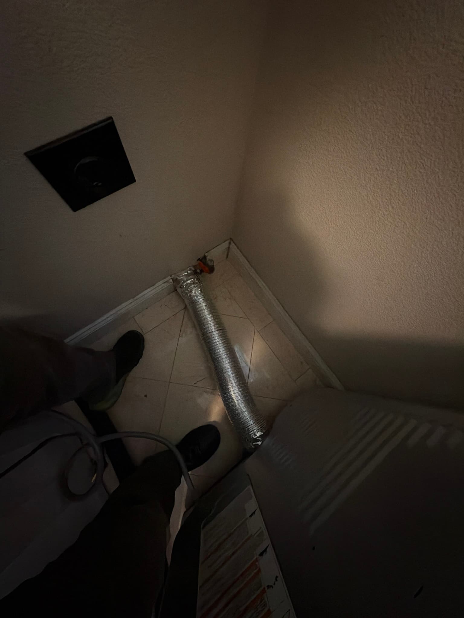 Low angle view of the newly installed DryerFlex transition duct running along the floor behind the dryer, connected at the wall exhaust outlet in the corner.