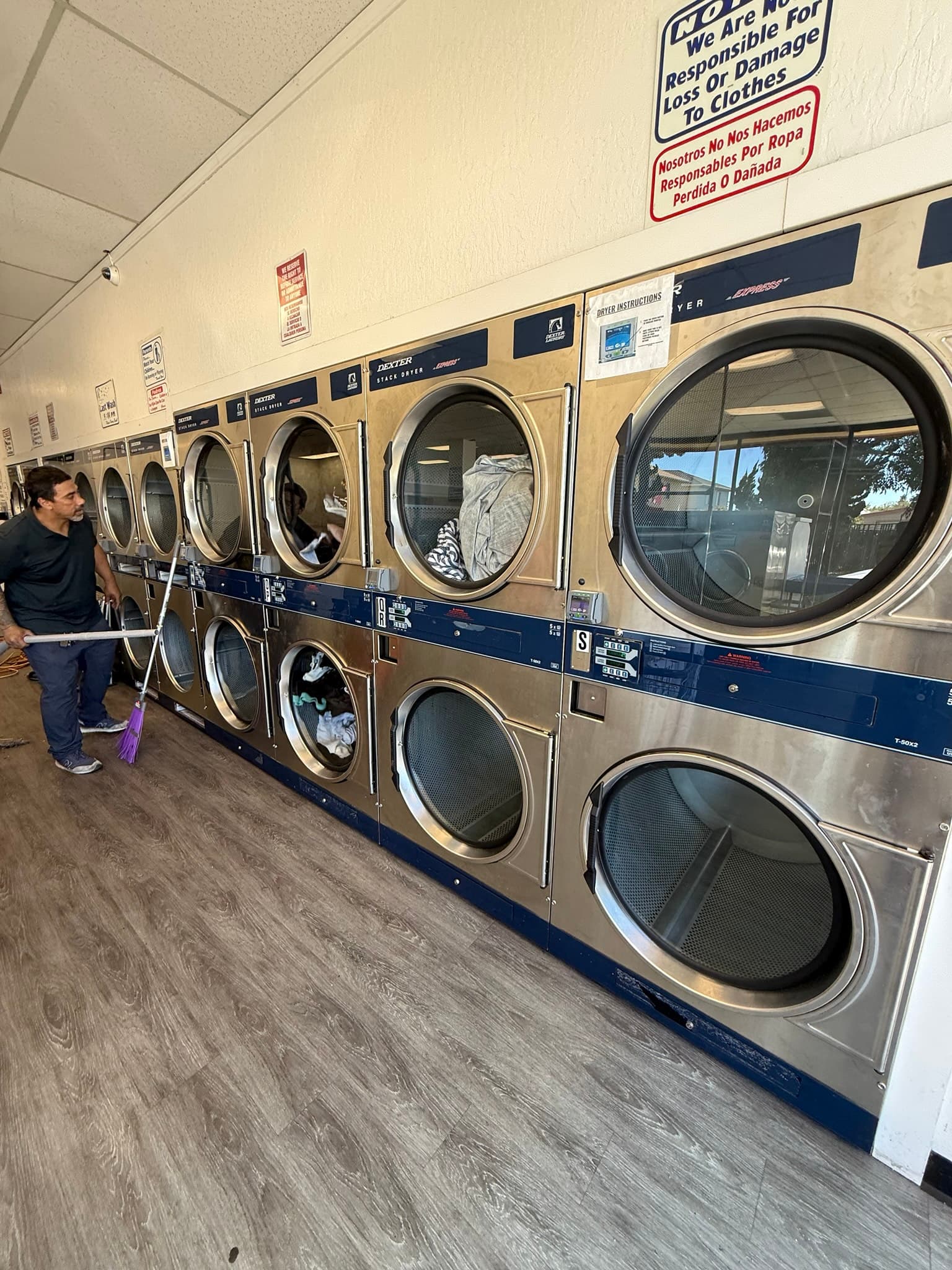 Interior of a commercial laundromat showing multiple stacked coin-operated dryers in rows, with instructional signage on the wall above the machines and laundry visible through some dryer doors