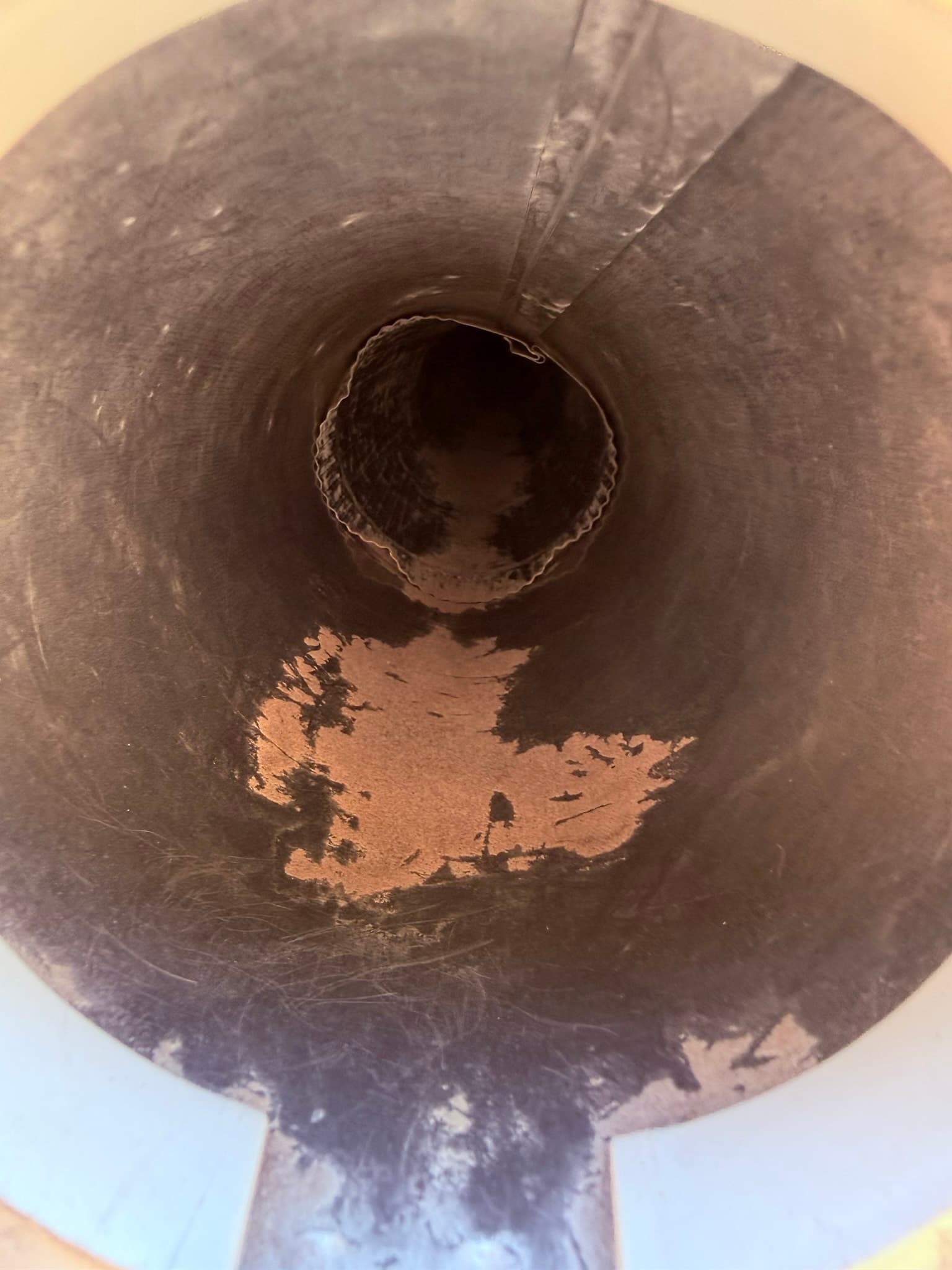 Interior view of a flexible dryer duct showing thick gray and tan lint deposits coating the inner duct walls and a connection point at center, demonstrating the degree of lint accumulation present before cleaning.