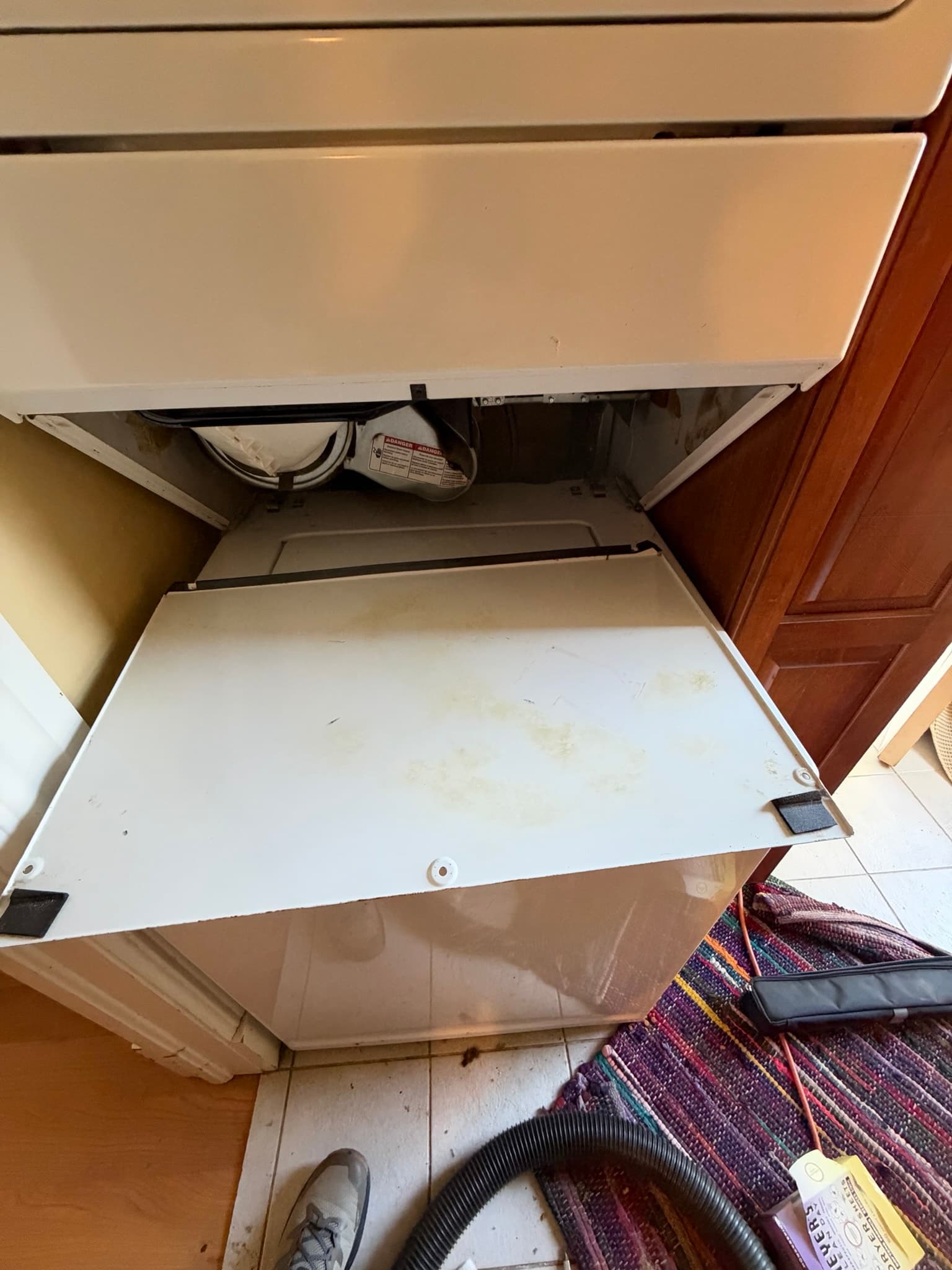 Dryer back panel pulled open exposing the internal duct connection and periscope vent routing with a shop vacuum hose staged for cleaning