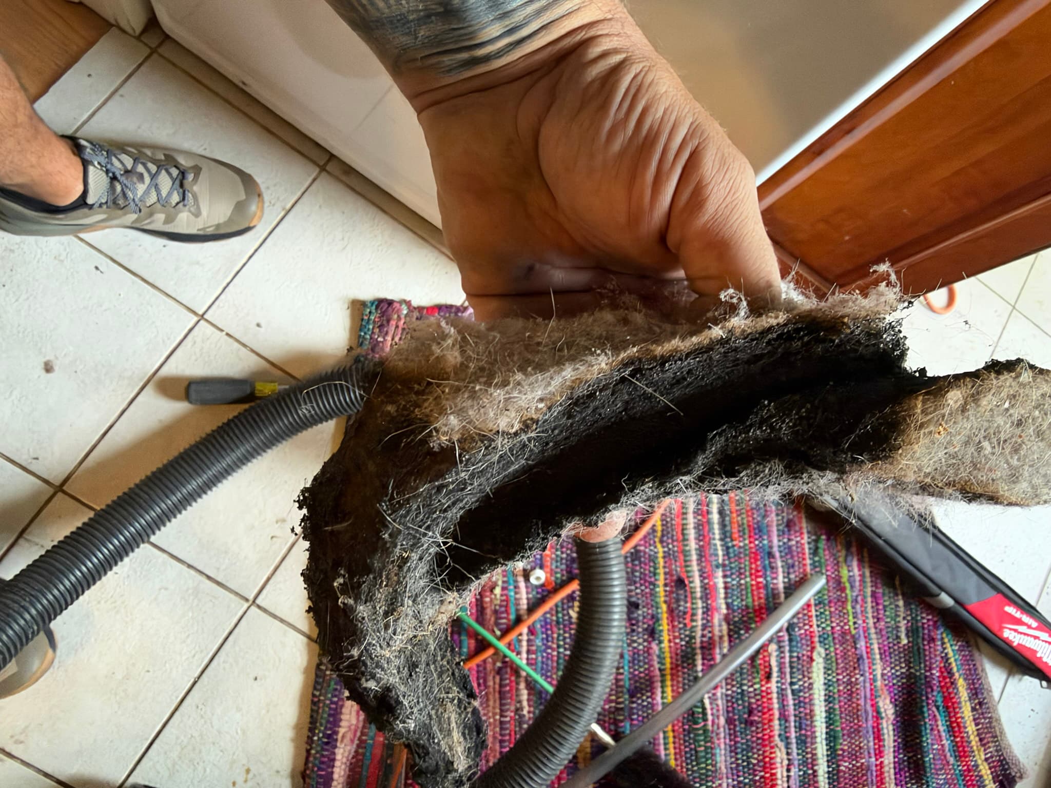 A dense, matted sheet of lint with a charred black core pulled by hand from the dryer exhaust duct before brush and vacuum cleaning