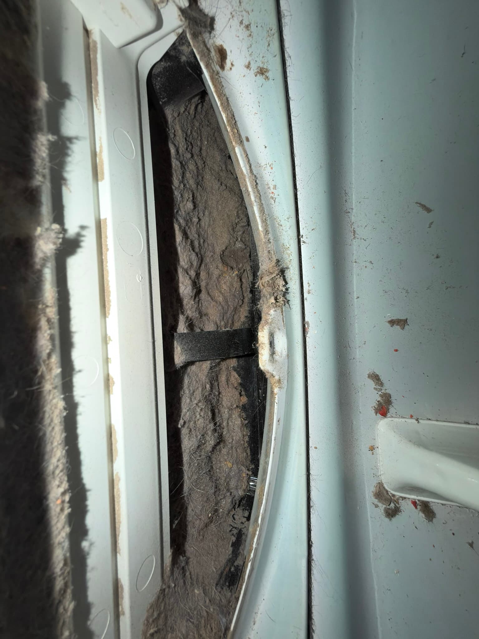 Lint trap housing packed solid with compacted lint along its full length, with heavy buildup also caked across the surrounding back panel edges