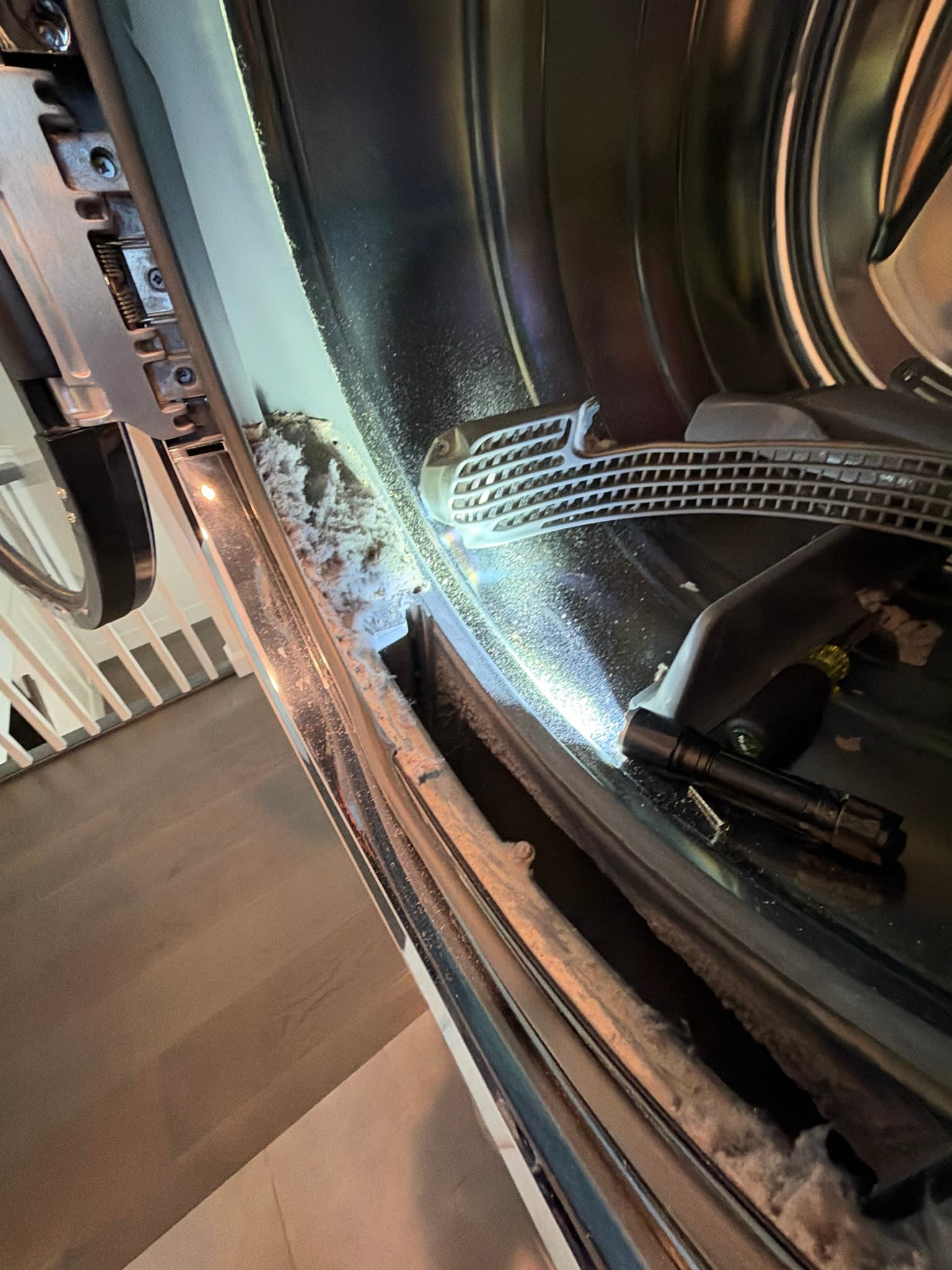 Interior of the dryer cabinet with front panel removed, showing the drum, belt, and lint packed along the rear vent grille seams