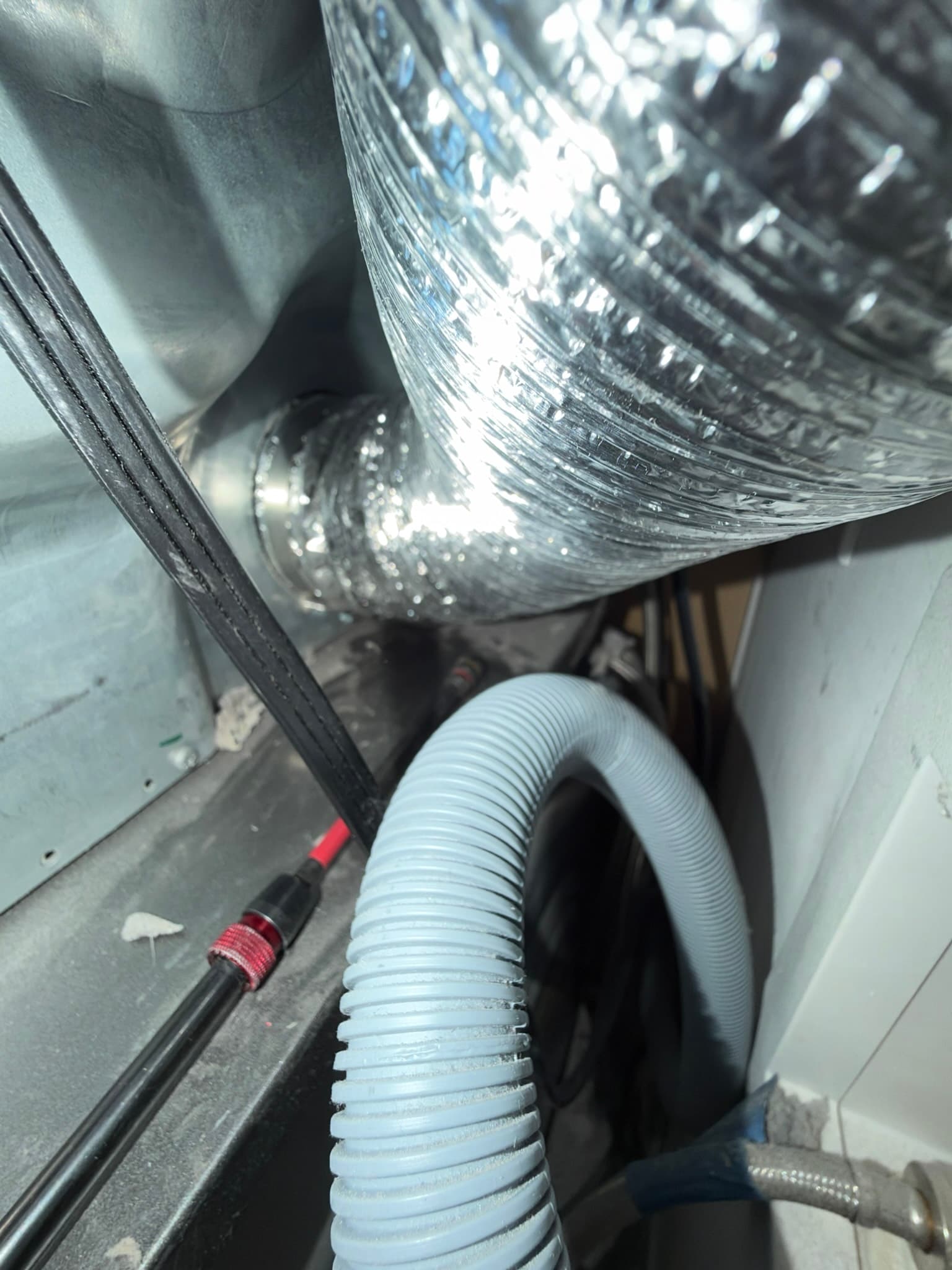 Close-up of the transition duct connection behind the dryer with a rotary brush cleaning tool visible during the cleaning process