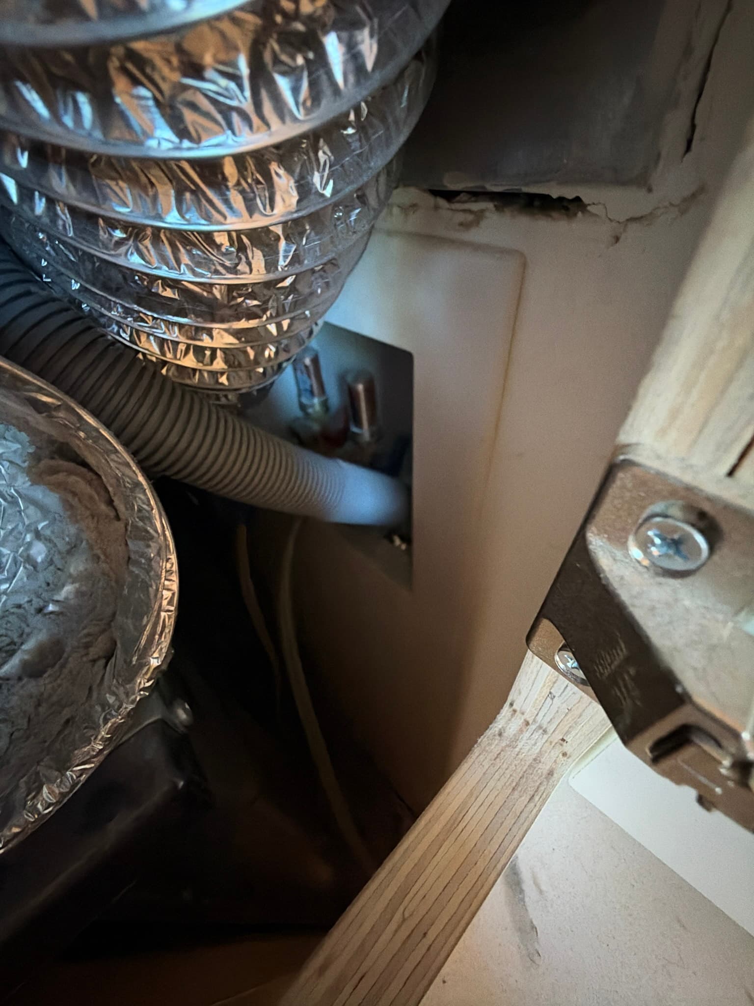 Dryer pulled from the wall exposing the foil transition duct with flattened sections in a tight appliance nook