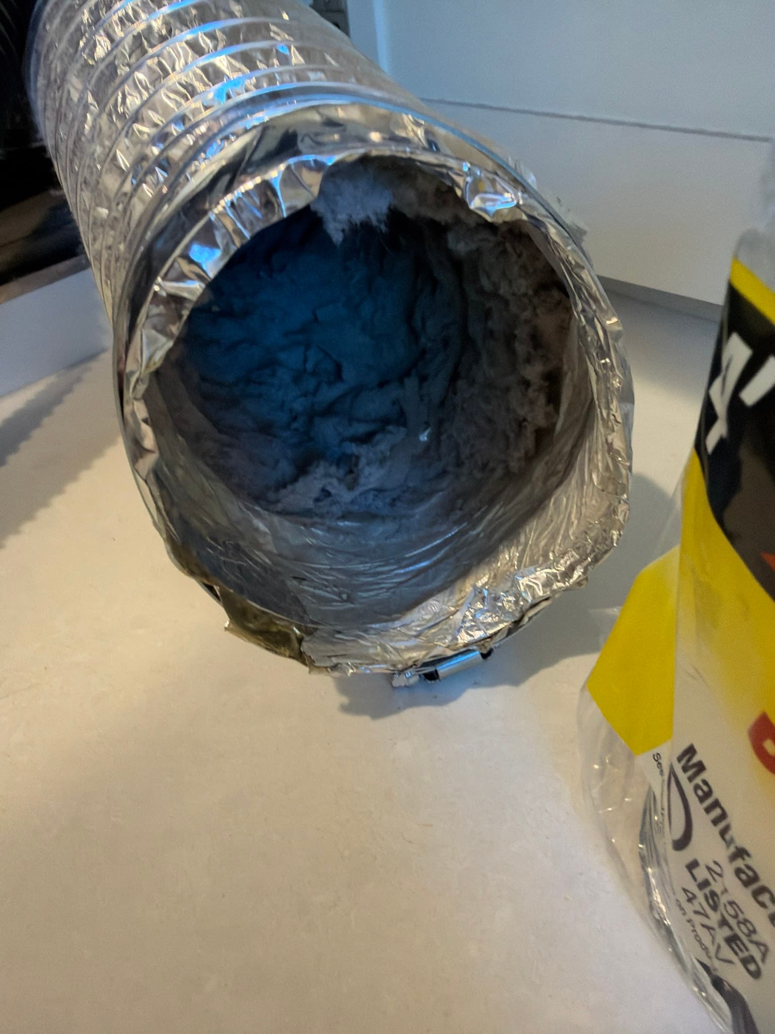 Disconnected foil transition duct with interior packed with heavy lint buildup before replacement