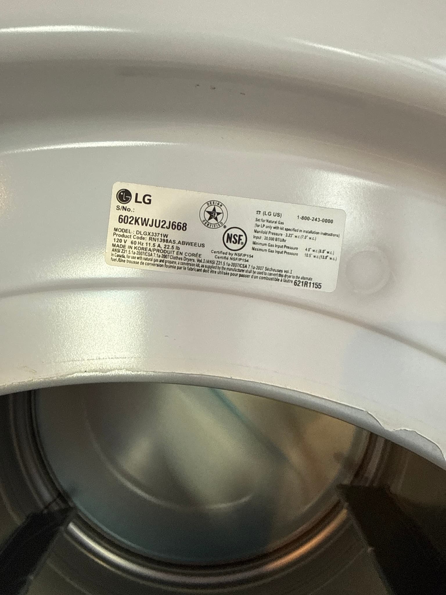Manufacturer specification label on the top of an LG gas dryer model DLGX331M, showing voltage rating of 120V, frequency of 60 Hz, and NSF certification marks on a clean white enamel surface