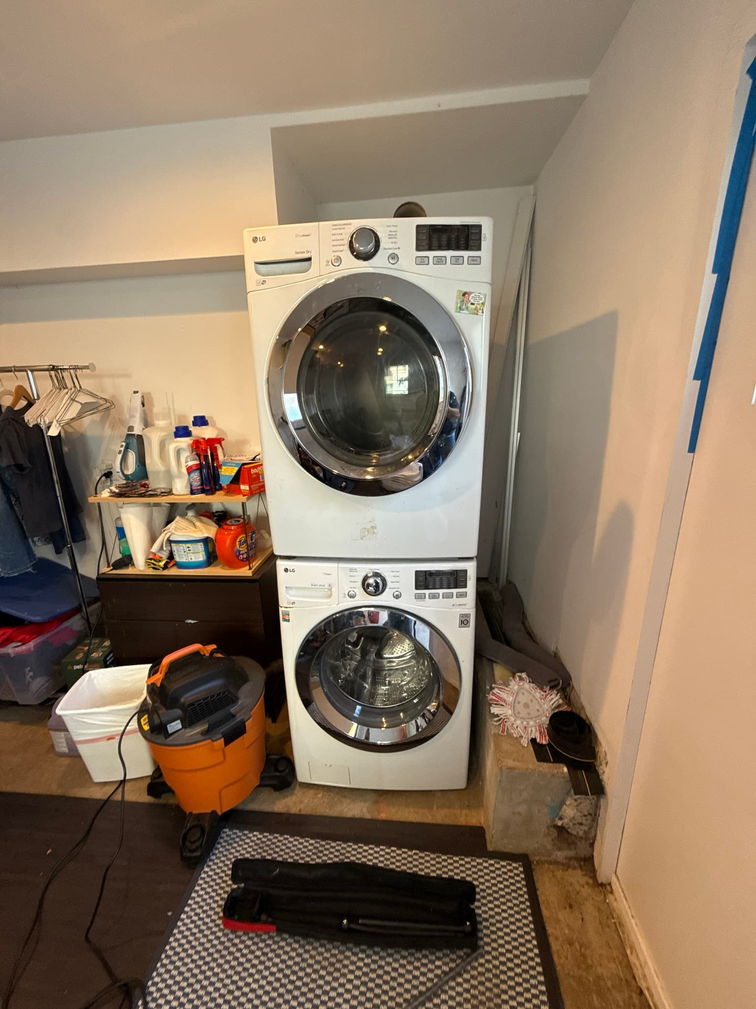 Stacked front-load washer and dryer units in a residential laundry closet with laundry supplies and cleaning equipment stored nearby