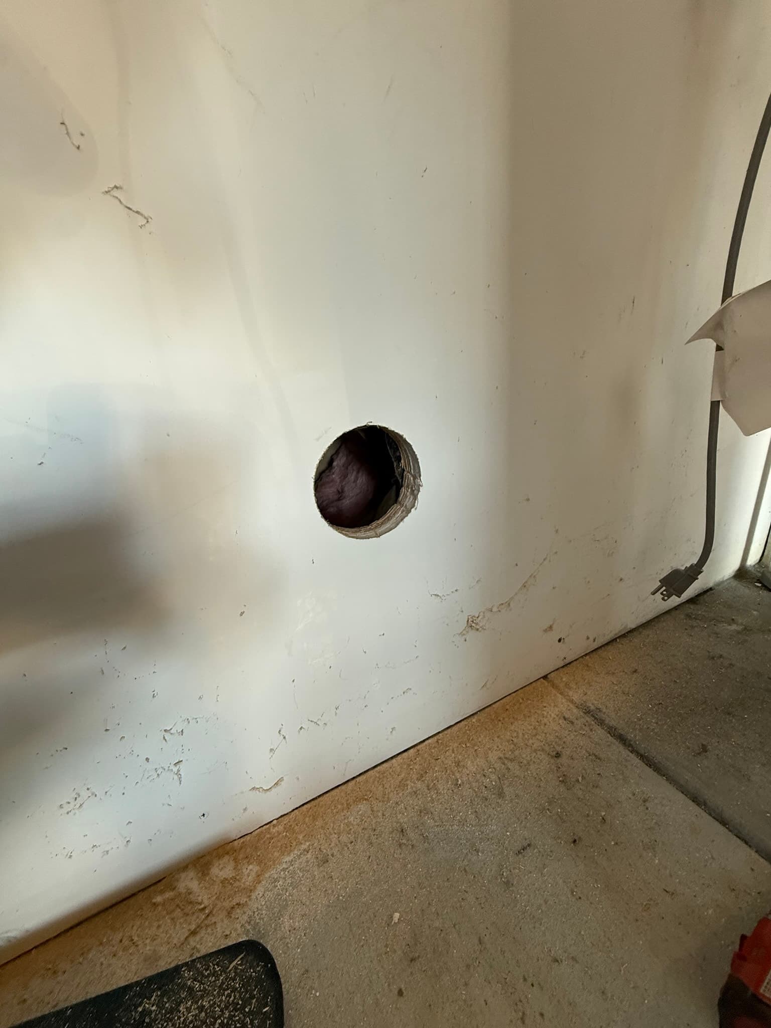 Initial wall penetration in progress showing the core-drilled opening through 5/8-inch drywall and 5/8-inch shear plywood on the interior wall, with the corresponding penetration made through the exterior stucco siding for the new dryer exhaust duct