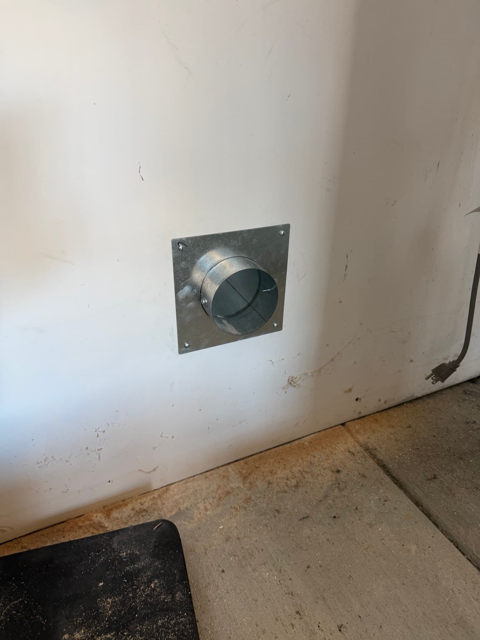 Newly installed dryer exhaust exit point showing approximately 12 inches of 26-gauge rigid galvanized pipe inside the wall, an 8-inch flat 28-gauge wall plate at the interior face, and the InOvate vent hood on the exterior stucco