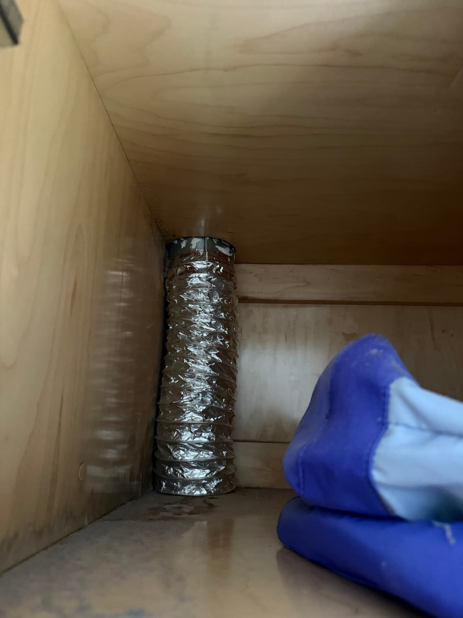 Interior view of the dryer cabinet showing a flexible black vent duct connected to the back panel with metal band clamps, with typical dust accumulation visible on interior surfaces around the dryer outlet