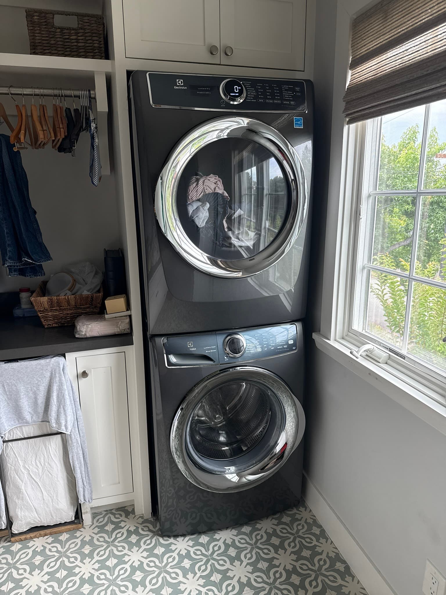 Stacked Electrolux front-load washer and dryer unit installed in a residential laundry closet with overhead cabinetry and storage baskets