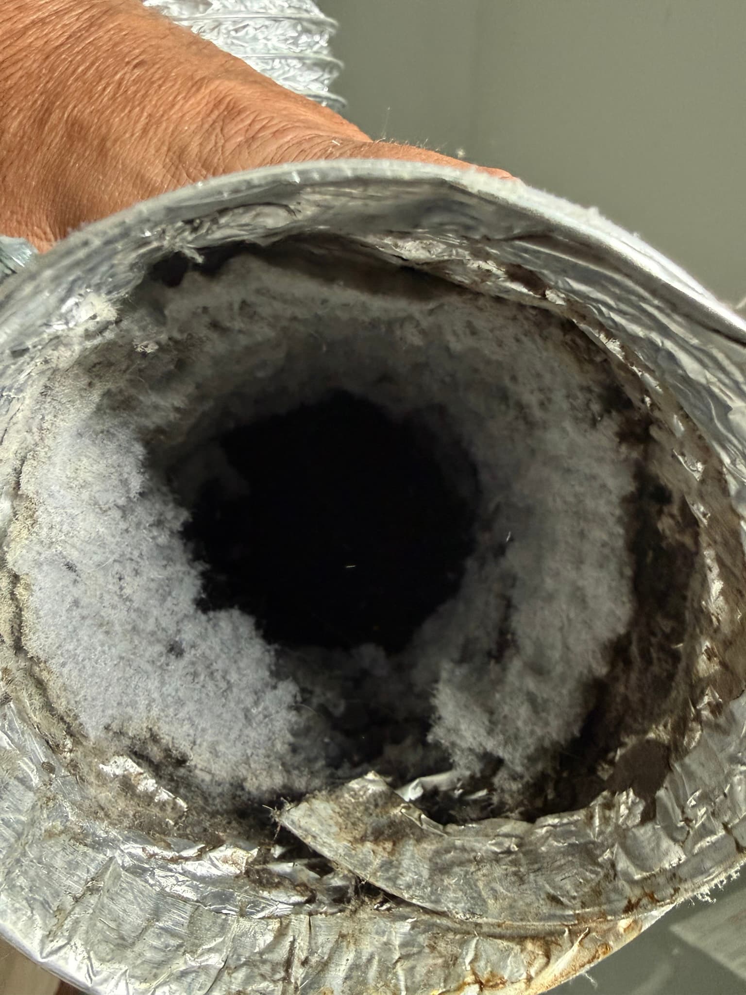 Interior view of a flexible dryer vent duct heavily clogged with thick, compacted gray and dark lint coating the duct walls and significantly narrowing the airflow passage