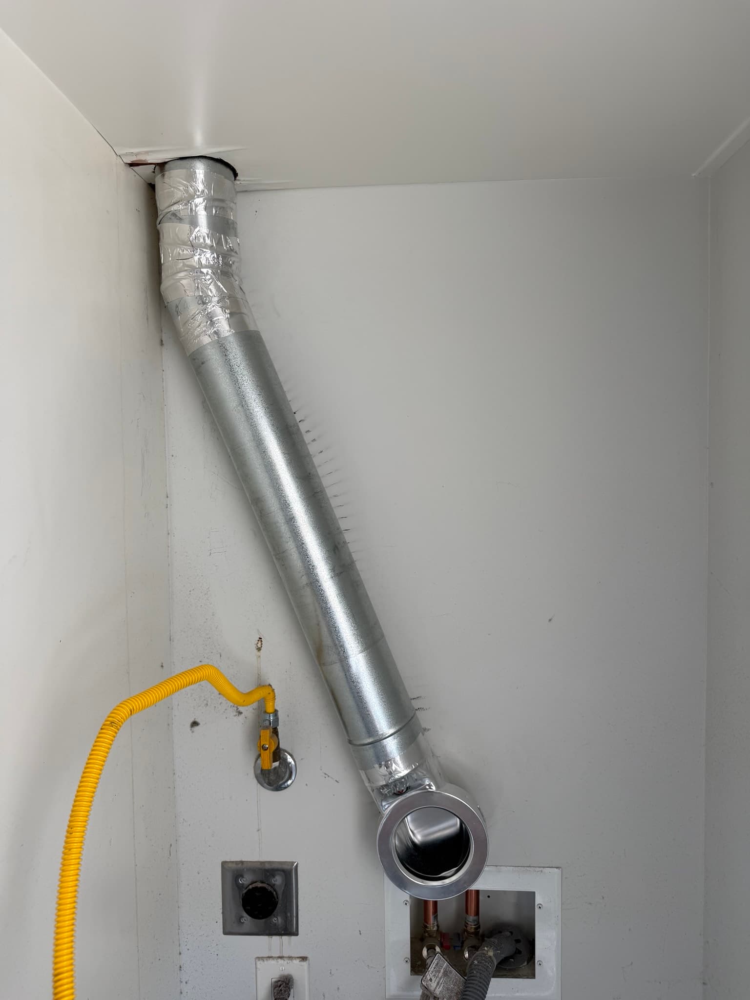 Completed magnetic vent connector and rigid hard pipe installation behind a stacked washer and dryer unit in a residential laundry closet, showing approximately 4 feet of straight pipe with a low-angle elbow