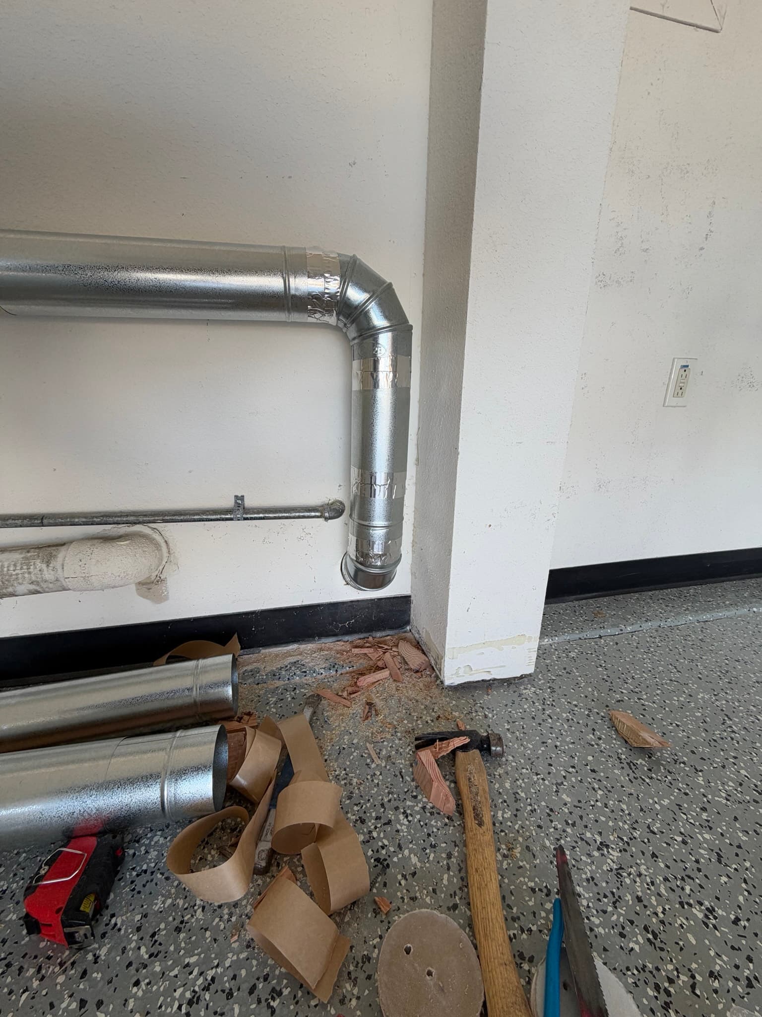 Newly installed run of 4 inch 26 gauge galvanized snap lock rigid duct with a 90 degree elbow and foil taped joints, sloped toward the exterior wall vent.