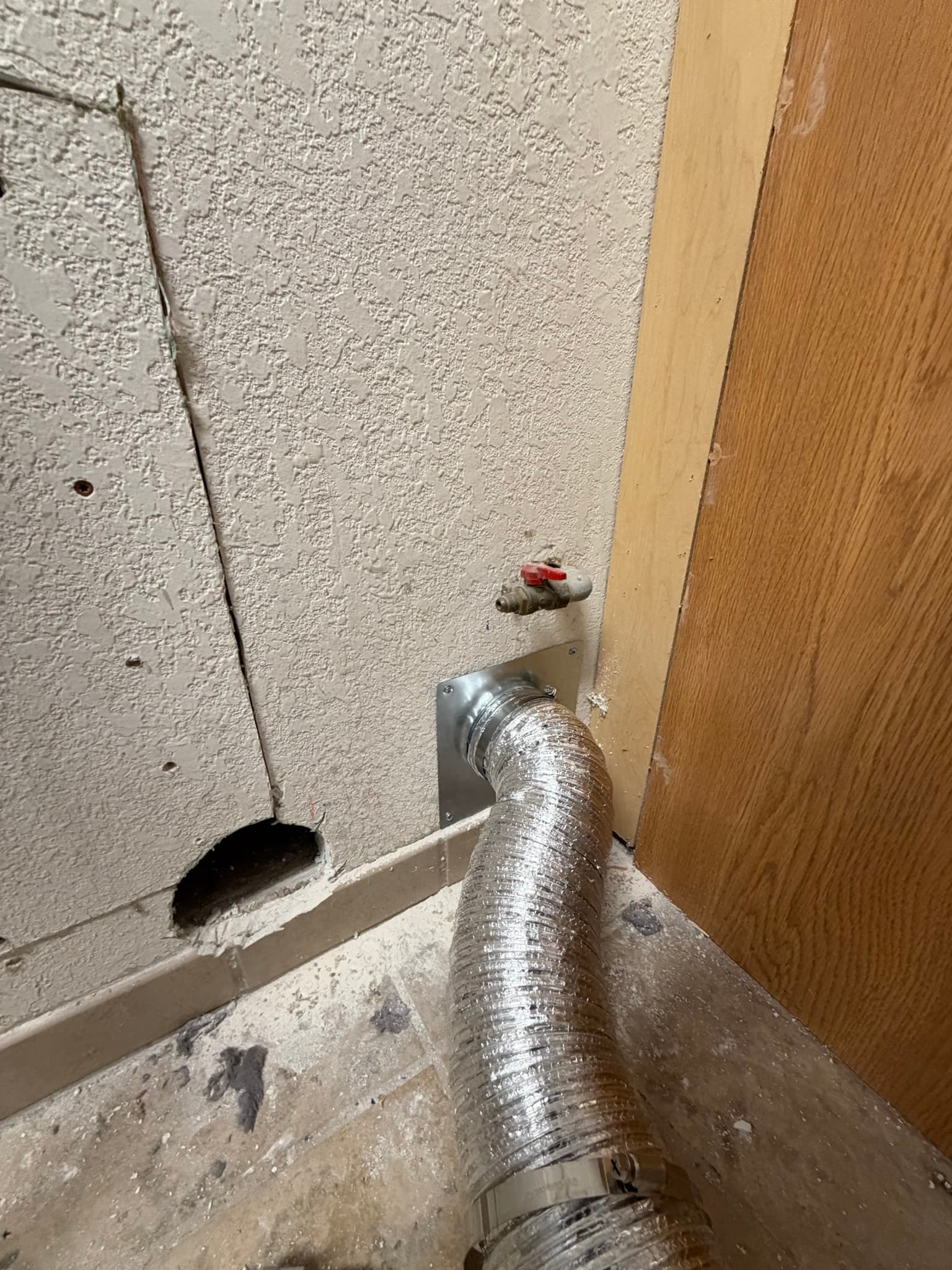 Interior wall connection showing DryerFlex transition duct clamped to a metal wall collar where the rigid duct passes through the wall to the exterior vent.