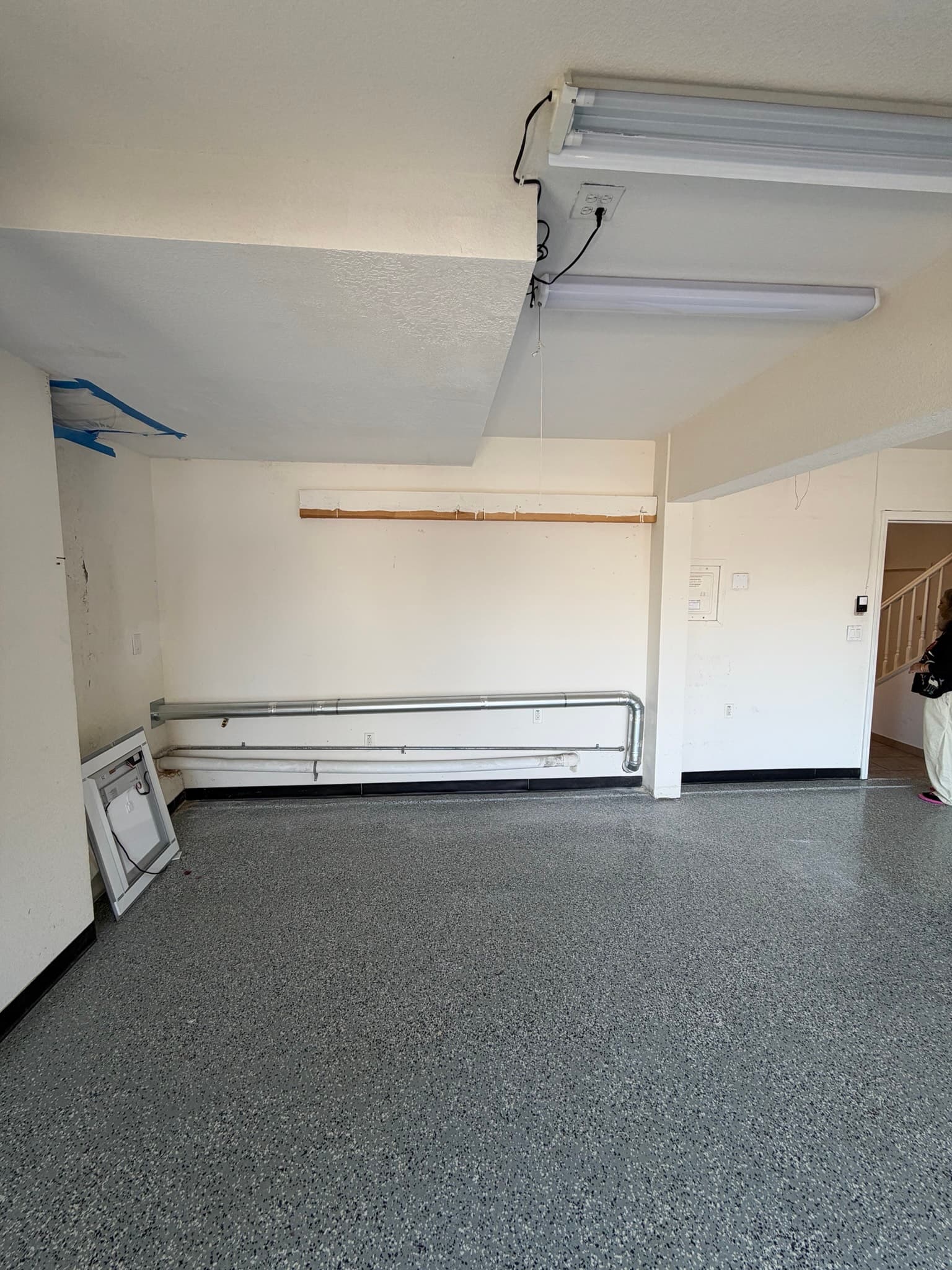 Completed dryer exhaust installation in a Redwood City garage showing rigid metal duct running along the lower wall with a proper downward slope toward the exterior wall vent outlet.
