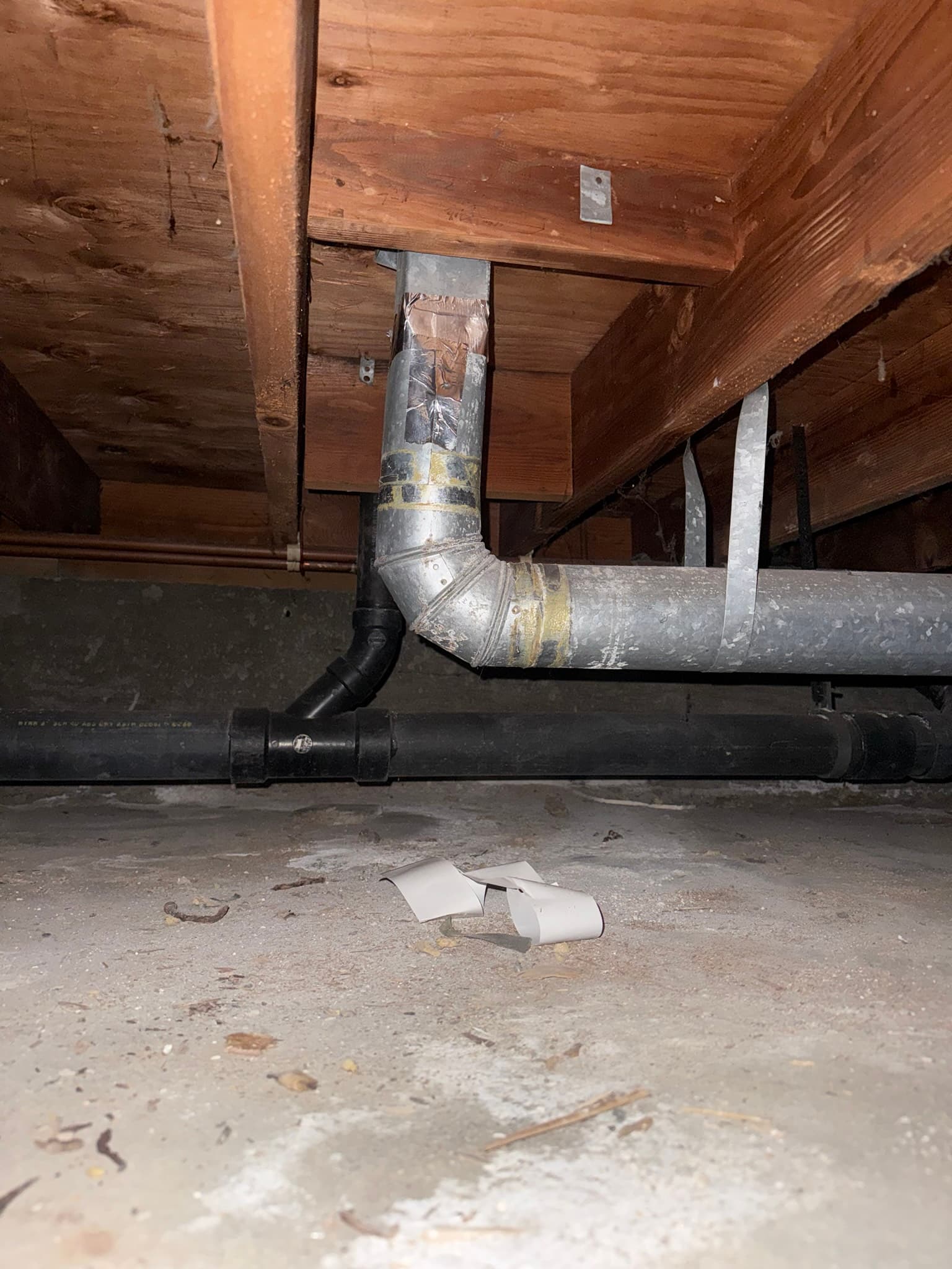 Crawl space duct system showing a galvanized metal supply duct with tape sealing and metal bands, a black transition fitting connecting to a flex duct section, and sagging unsupported horizontal duct runs beneath aged wooden joists