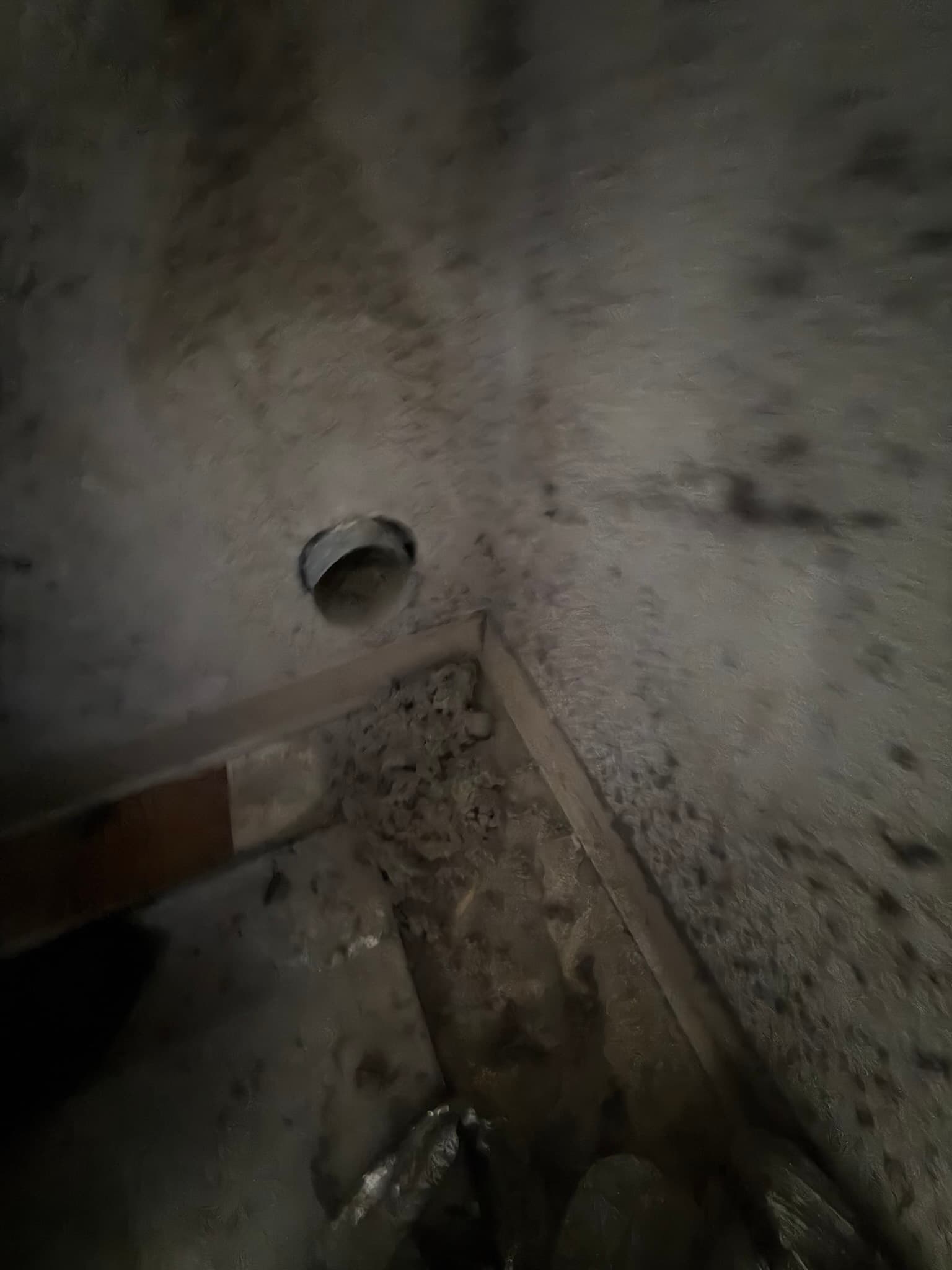 Confined wall cavity space showing thick lint buildup coating the floor and framing near a small metal dryer duct opening before cleaning