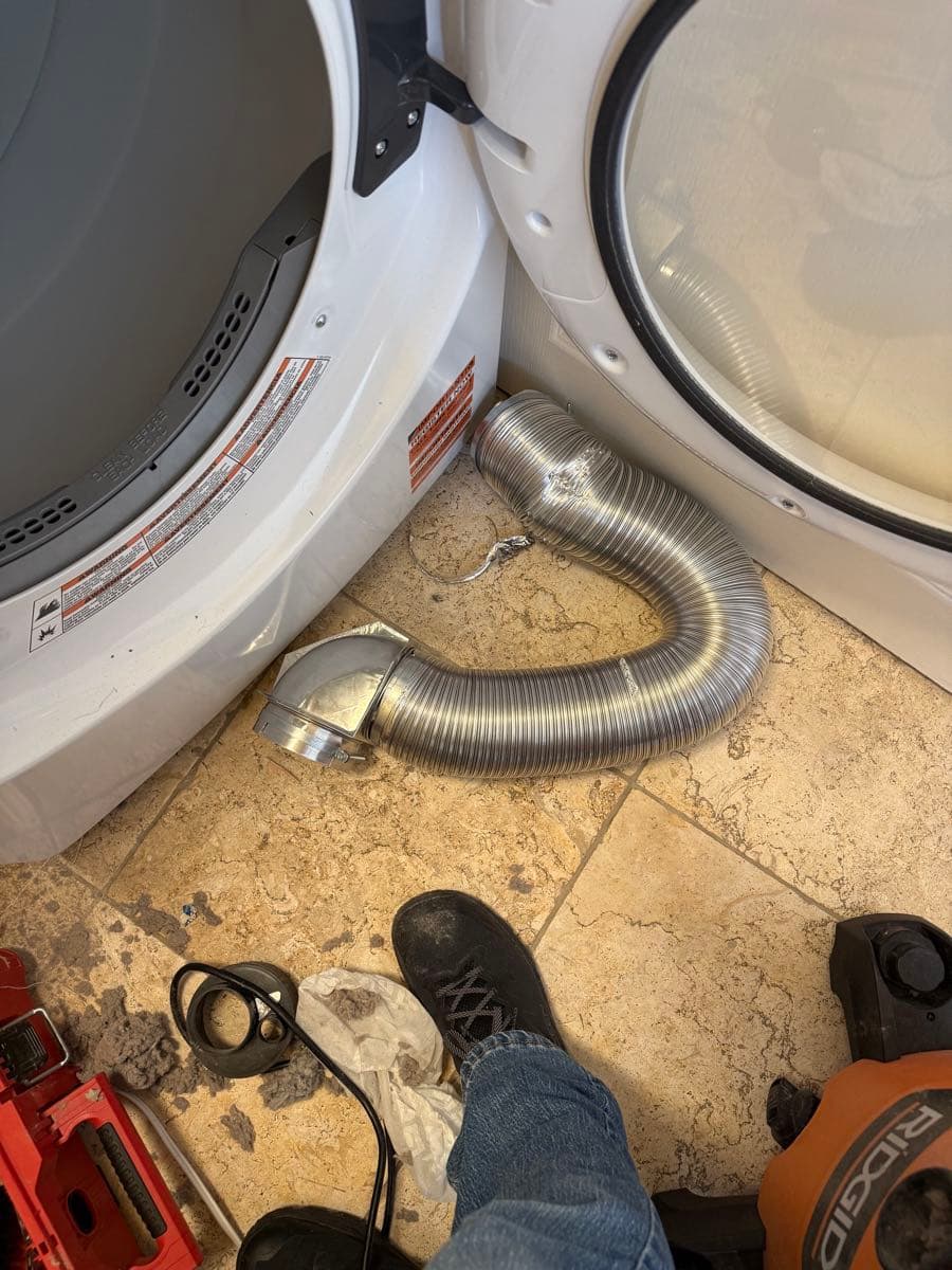 Oversized semi-rigid metal transition duct coiled and compressed behind the dryer, creating airflow restriction due to excessive length beyond the 8-foot code maximum