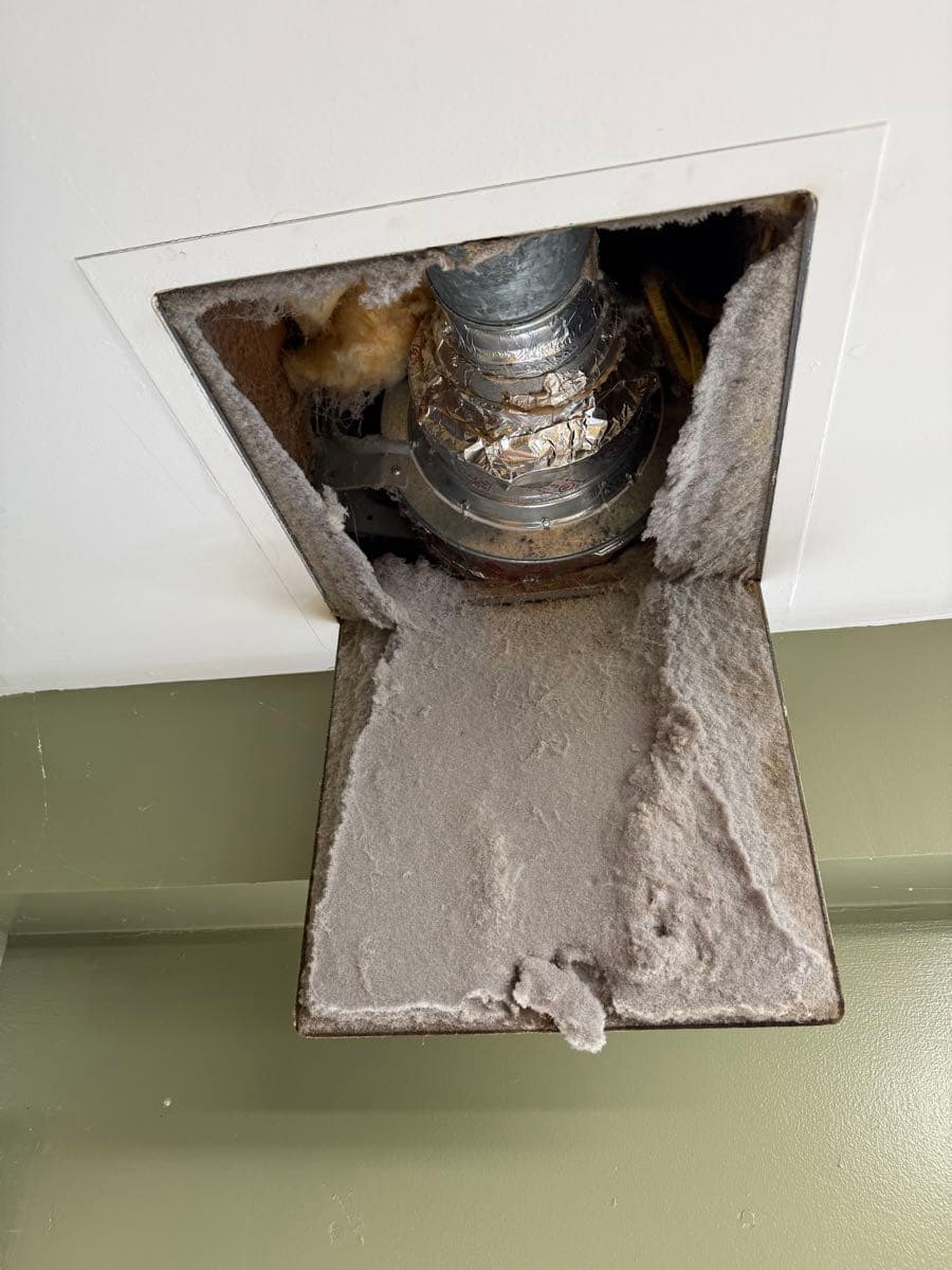 Non-compliant domestic booster fan mounted in the garage section of the dryer exhaust duct run, electrically disconnected and acting as a full airflow blockage and fire hazard
