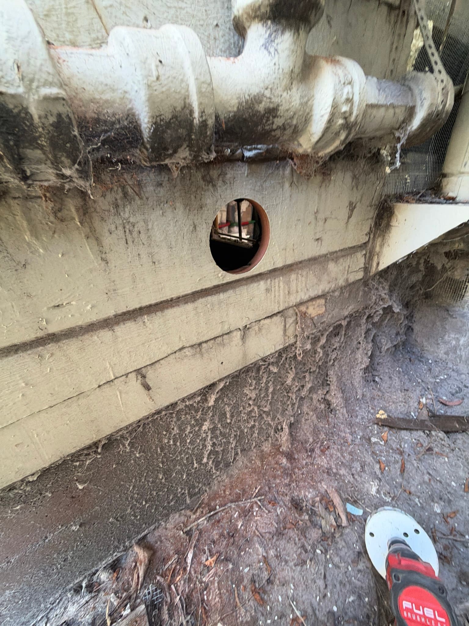 Freshly cored exterior wall opening with no vent cap installed yet, heavy lint caked on the siding and trim board below from prior exhaust leakage.