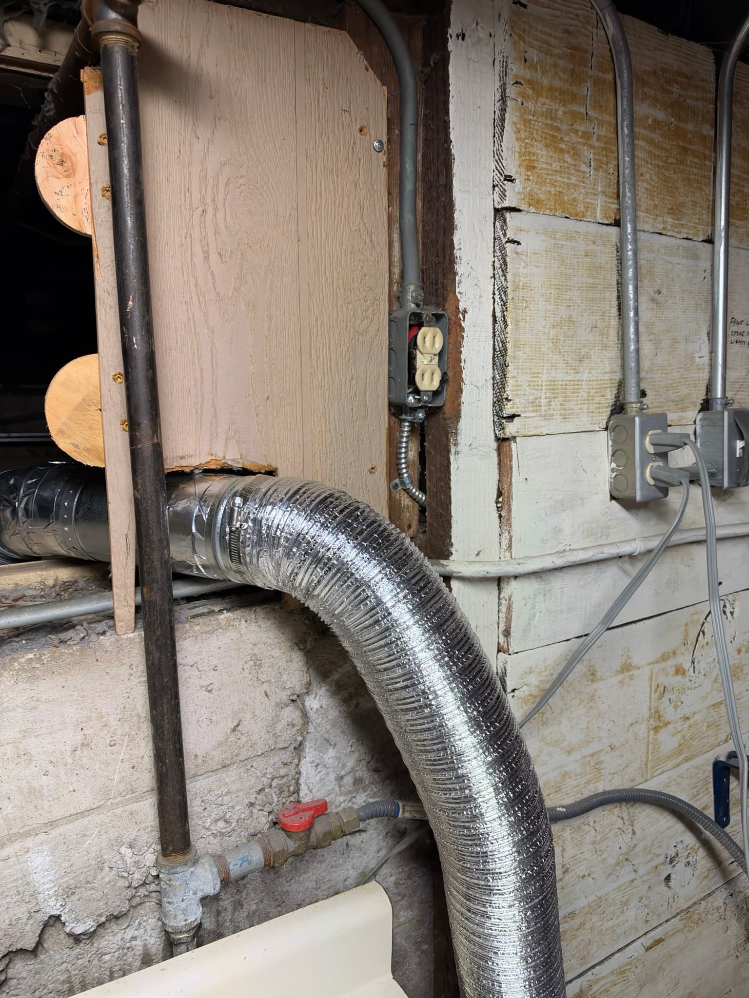 New 4 inch DryerFlex semi-rigid aluminum duct secured with a hose clamp connecting to rigid metal duct near wood backing board in a basement utility area.