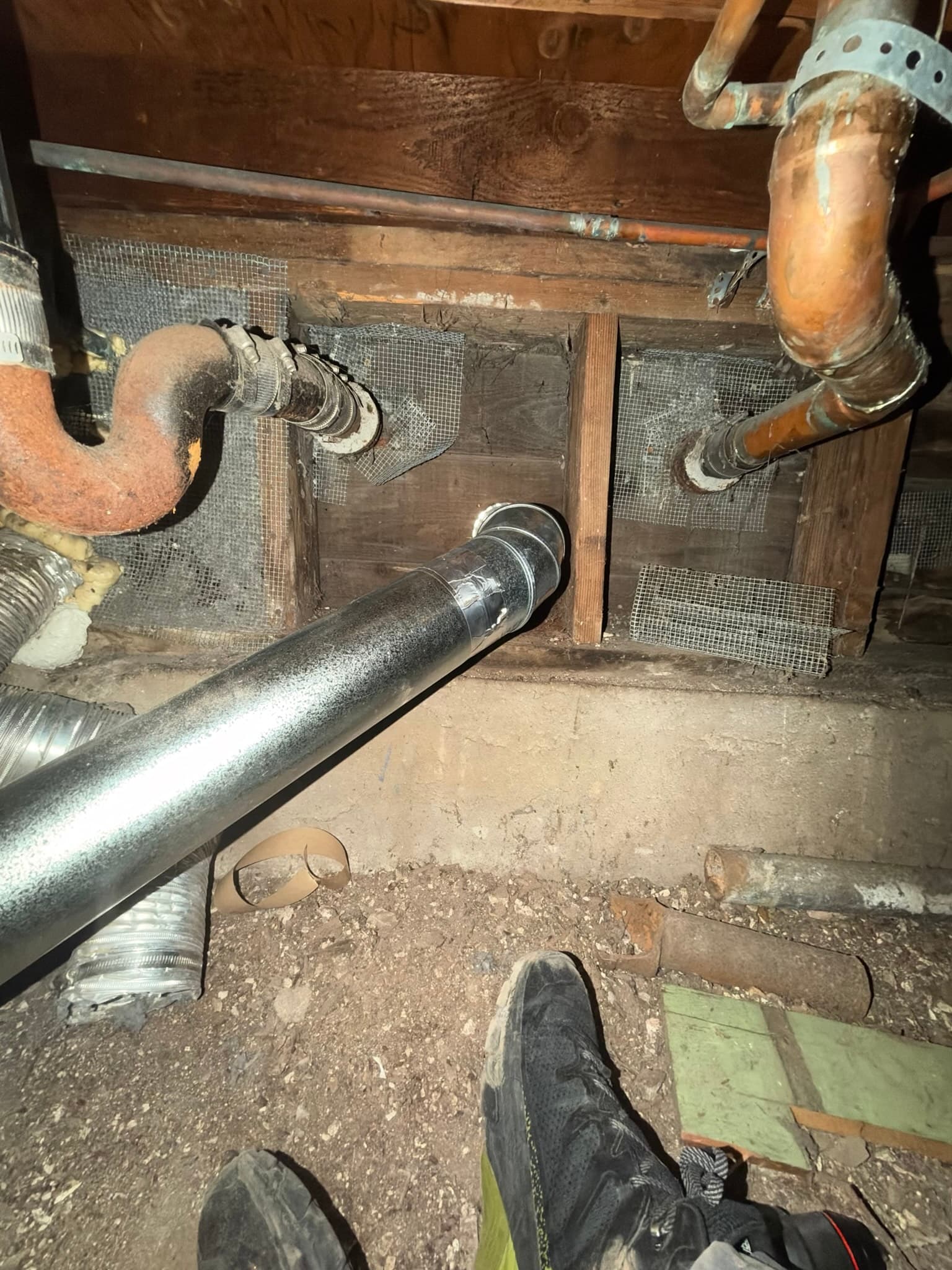 Rigid galvanized snap lock pipe running through crawlspace floor joists toward the exterior vent connection, taped at the seams.