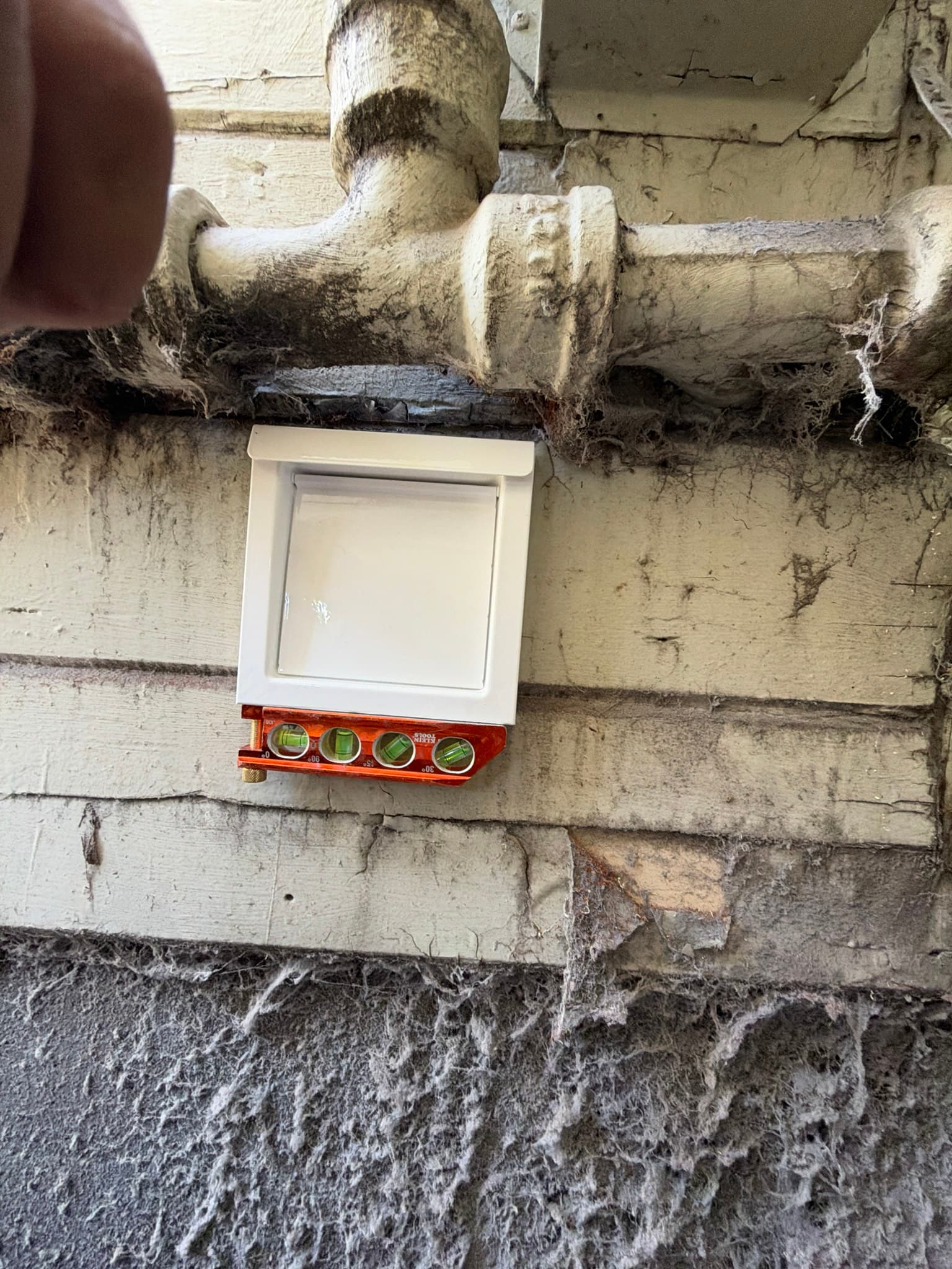 A newly installed DryerWallVent, 4" Flush Mount, No Collar, White is mounted flush on the exterior siding, with its damper closed and a level used to confirm proper alignment.