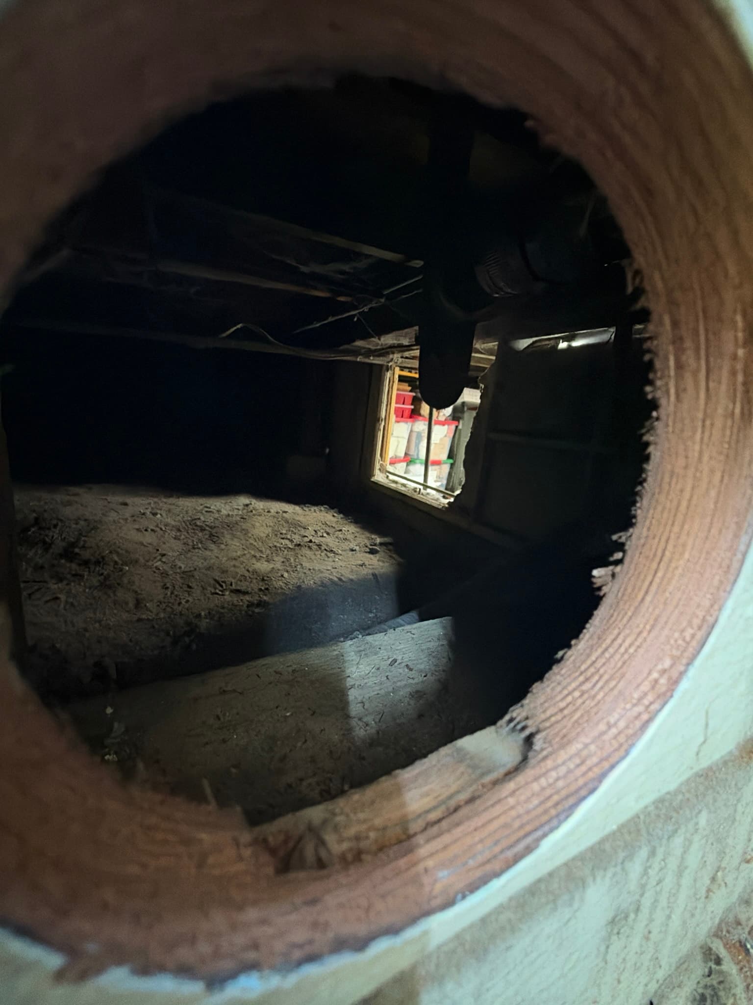 View through a bored exterior wall opening into the crawlspace below, with bare unfinished edges and no vent cap installed.