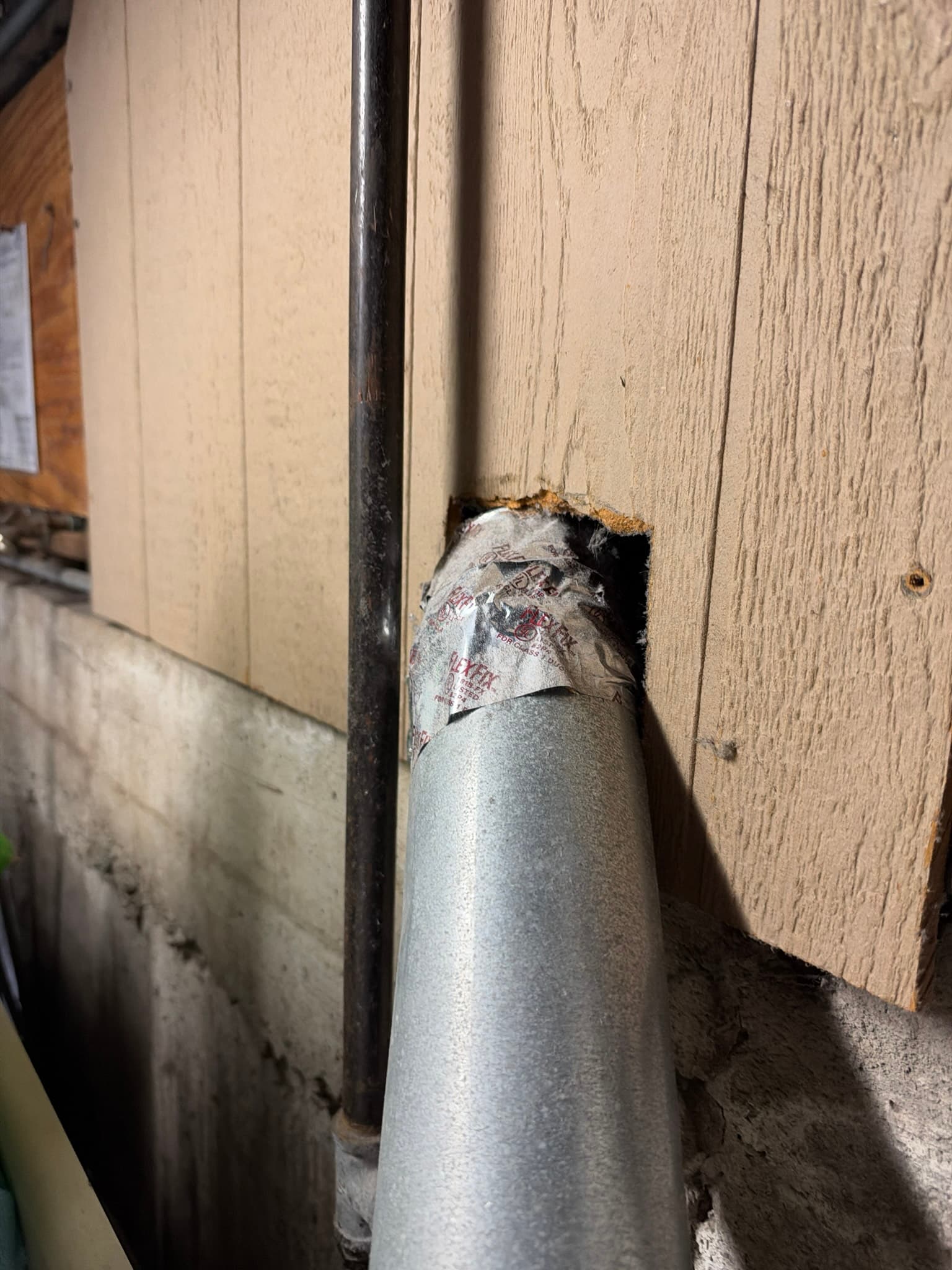 Rigid metal duct penetrating unfinished exterior siding with the joint wrapped in foil tape and no wall vent cap installed.