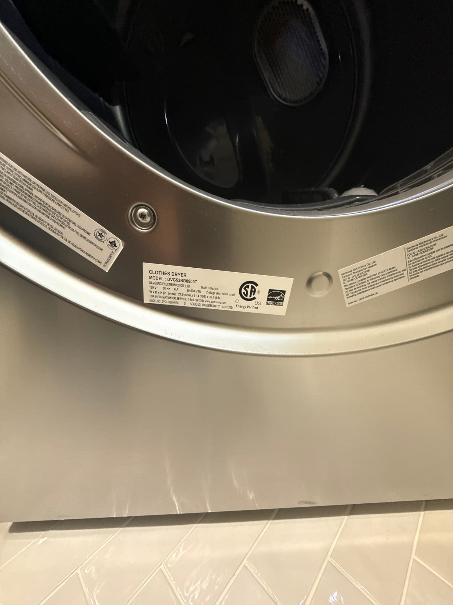 Rear panel of a stainless steel clothes dryer viewed from above, showing manufacturer certification labels including CSA and Energy Star markings, with no duct connections or exhaust components visible