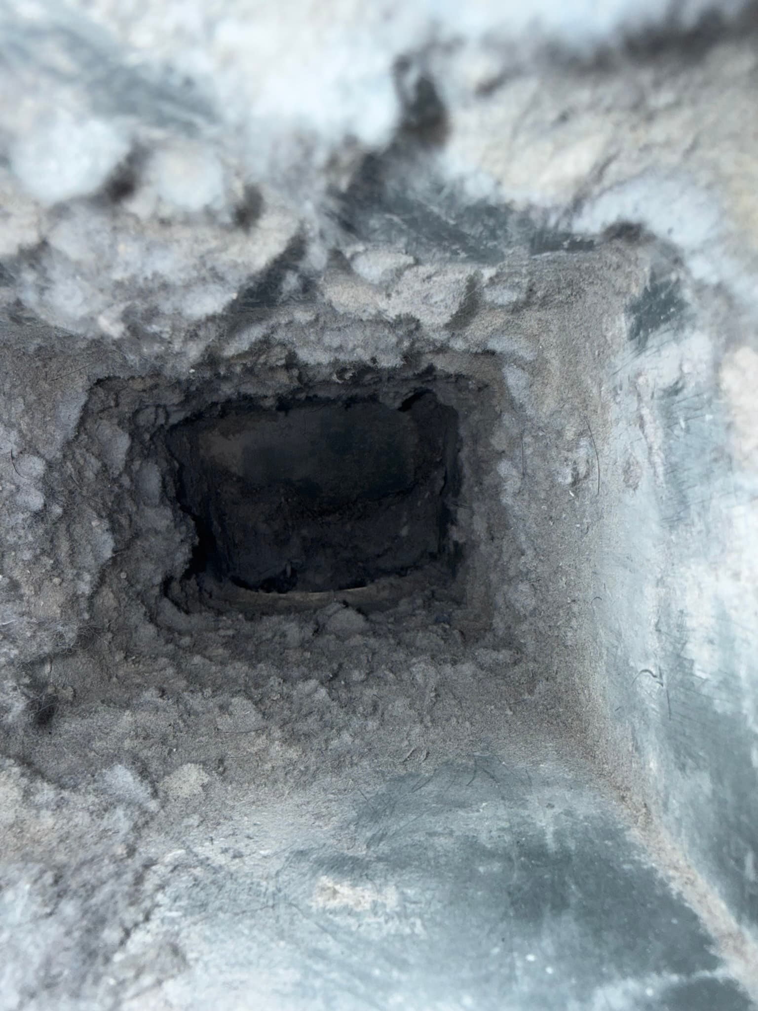 Interior view of a dryer exhaust duct severely clogged with compacted lint, showing a small dark central opening surrounded by thick, dense lint accumulation that nearly completely blocks airflow