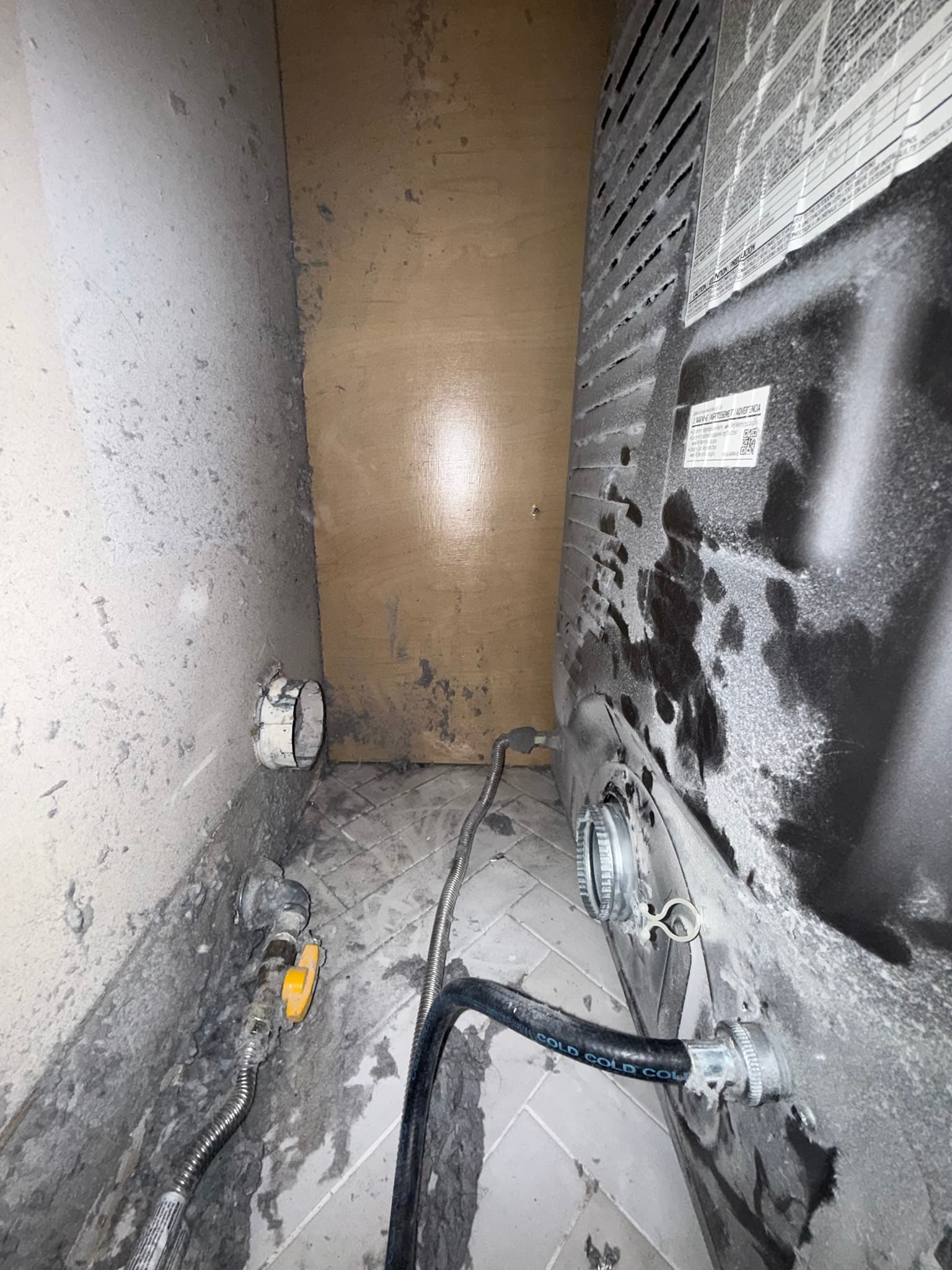 Dryer exhaust duct routed through a narrow wall cavity, with a black flexible duct secured by hose clamps connecting to a rigid metal elbow at the exterior wall, and heavy lint and dust deposits visible on surrounding wall surfaces and duct fittings