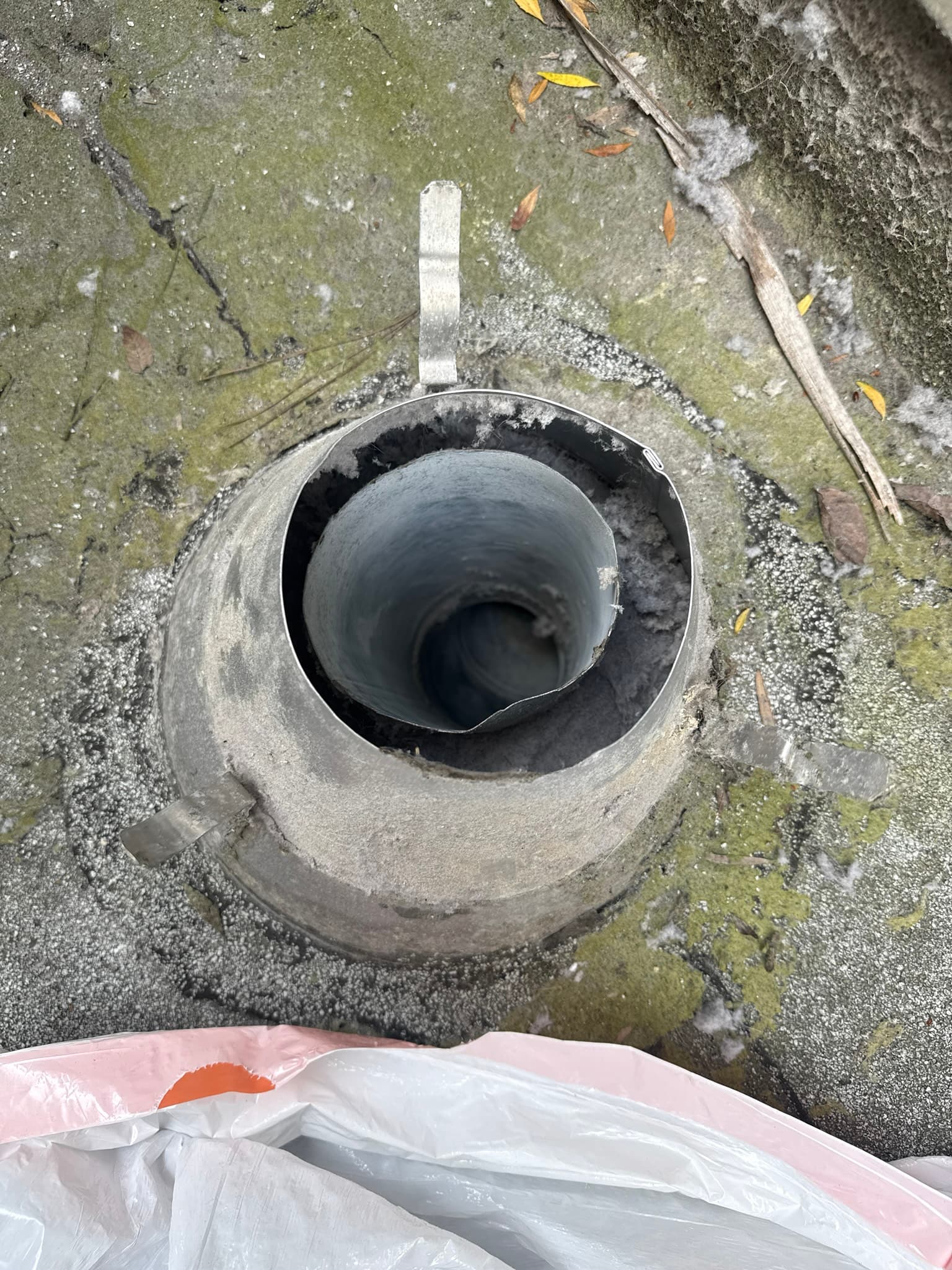 Exterior dryer vent cap on a moss-covered roof after cleaning, showing a clear periscope-style flapper opening with no visible lint blockage and verified sealed duct joints throughout the system