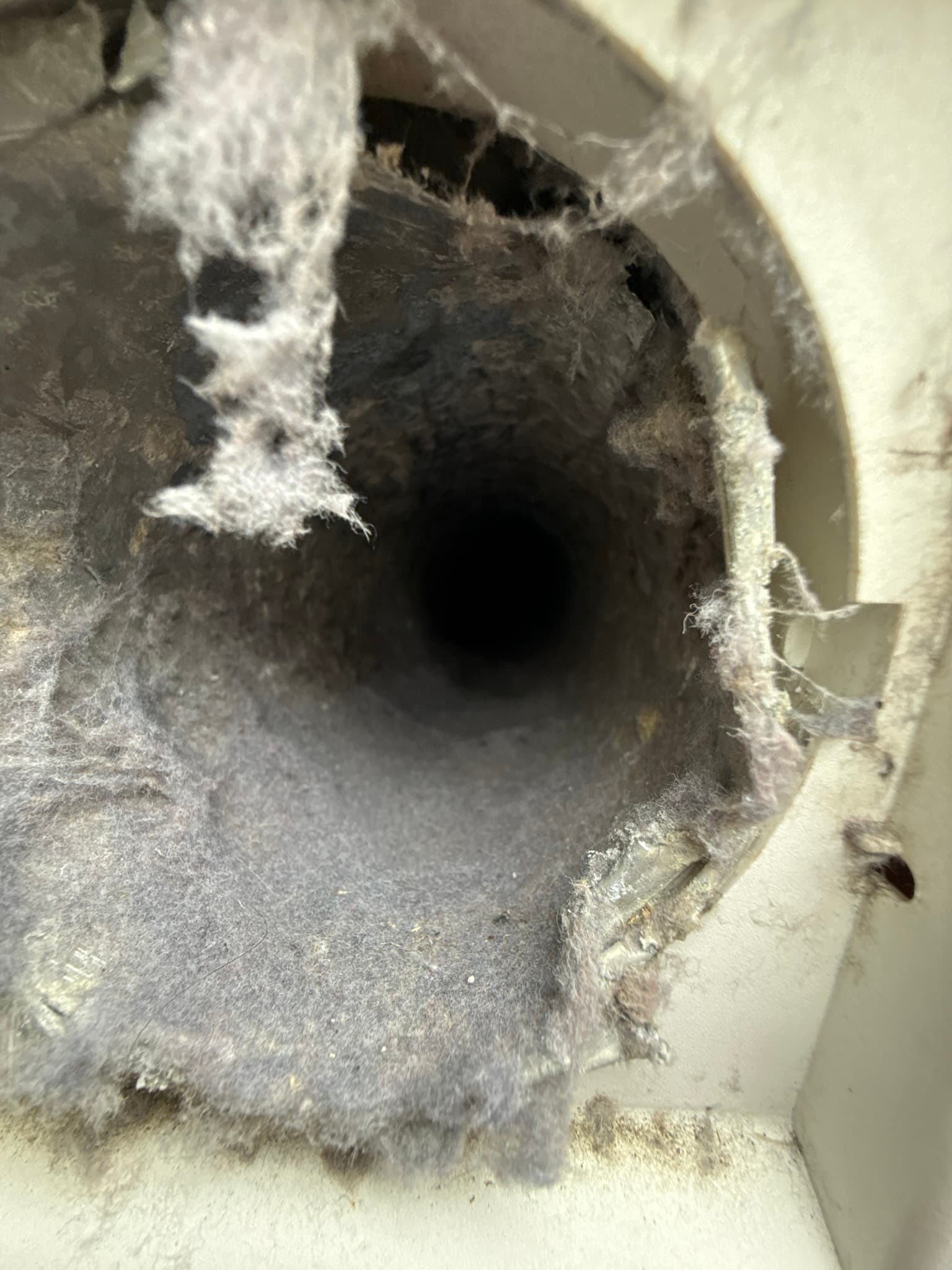 Close-up view of a dryer vent duct opening showing visible lint clogging the interior before cleaning service begins