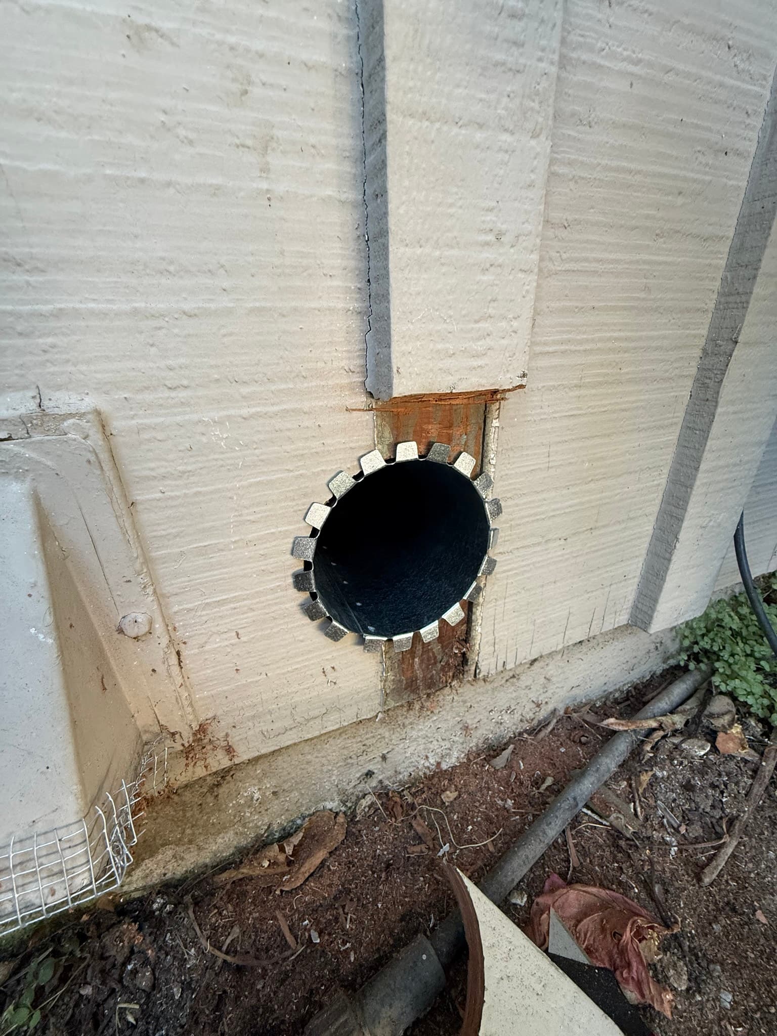 New exterior dryer vent cap mounted on a concrete foundation wall with a black flanged metal collar and perforated mounting flange at the wall penetration